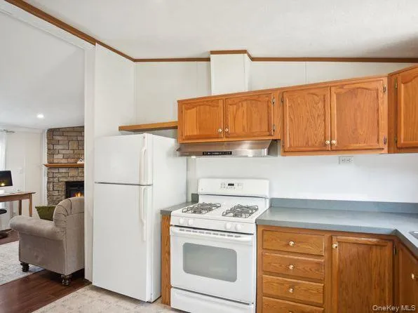 Kitchen with white appliances, brown cabinetry, a stone fireplace, ornamental molding, and light wood-type flooring Kitchen with white appliances, brown cabinetry, a stone fireplace, ornamental molding, and light wood-type flooring