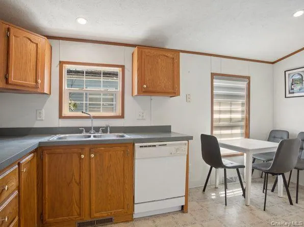 Kitchen featuring brown cabinets, dishwasher, ornamental molding, recessed lighting, and dark countertops Kitchen featuring brown cabinets, dishwasher, ornamental molding, recessed lighting, and dark countertops
