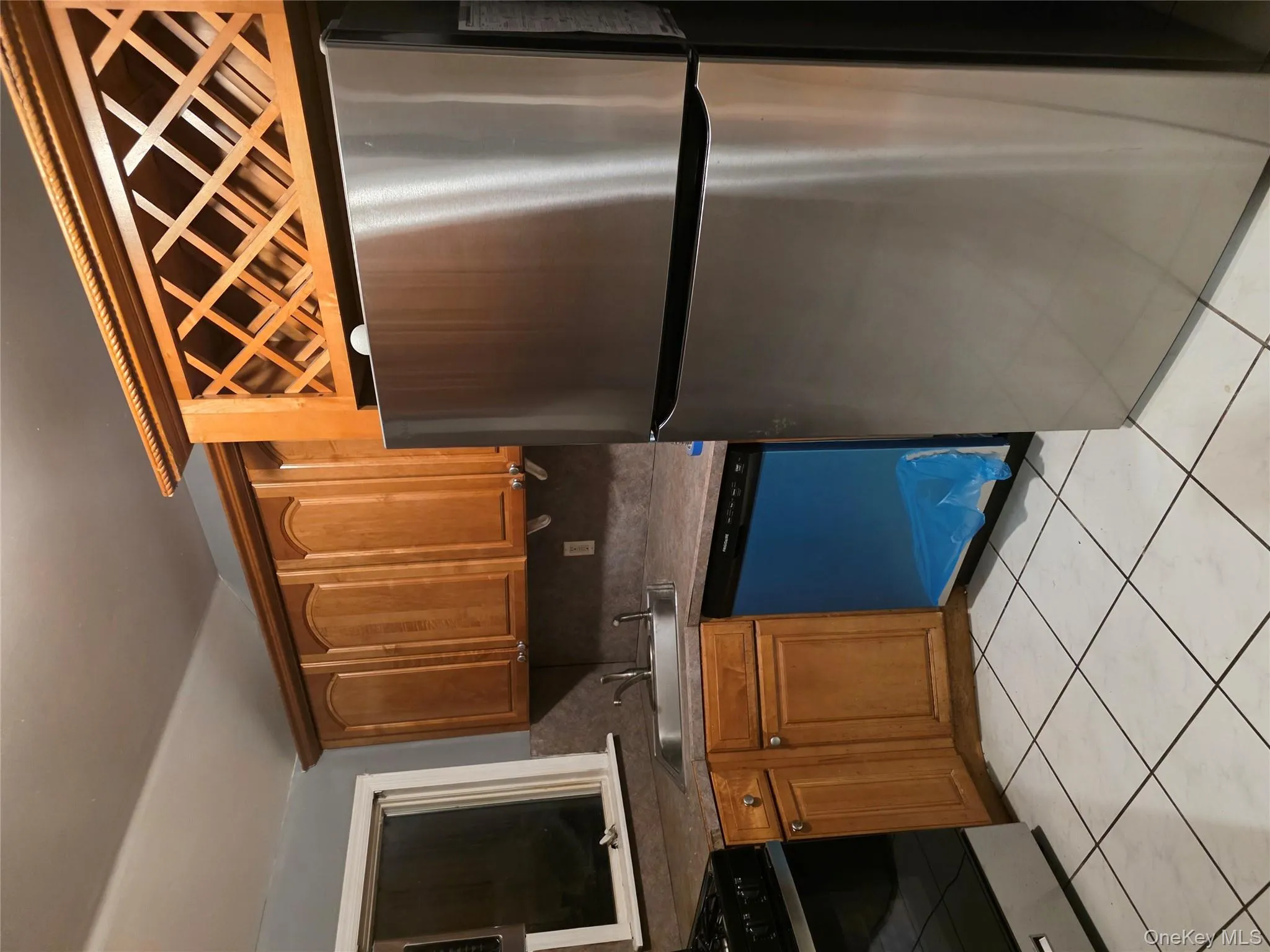 Kitchen featuring stainless steel refrigerator, stove, brown cabinetry, dishwashing machine, and light tile patterned floors Kitchen featuring stainless steel refrigerator, stove, brown cabinetry, dishwashing machine, and light tile patterned floors