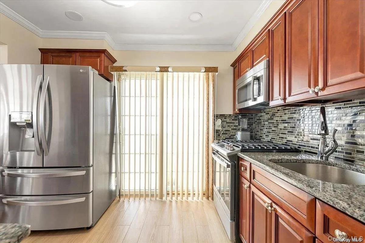 Kitchen with stainless steel appliances, dark stone counters, ornamental molding, light wood-style floors, and decorative backsplash Kitchen with stainless steel appliances, dark stone counters, ornamental molding, light wood-style floors, and decorative backsplash