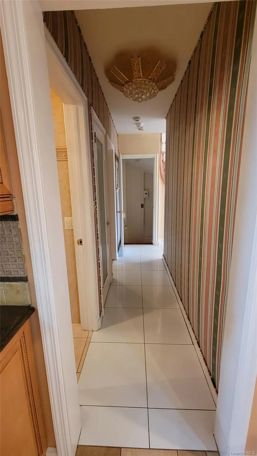 Hallway featuring light tile patterned flooring and wallpapered walls Hallway featuring light tile patterned flooring and wallpapered walls