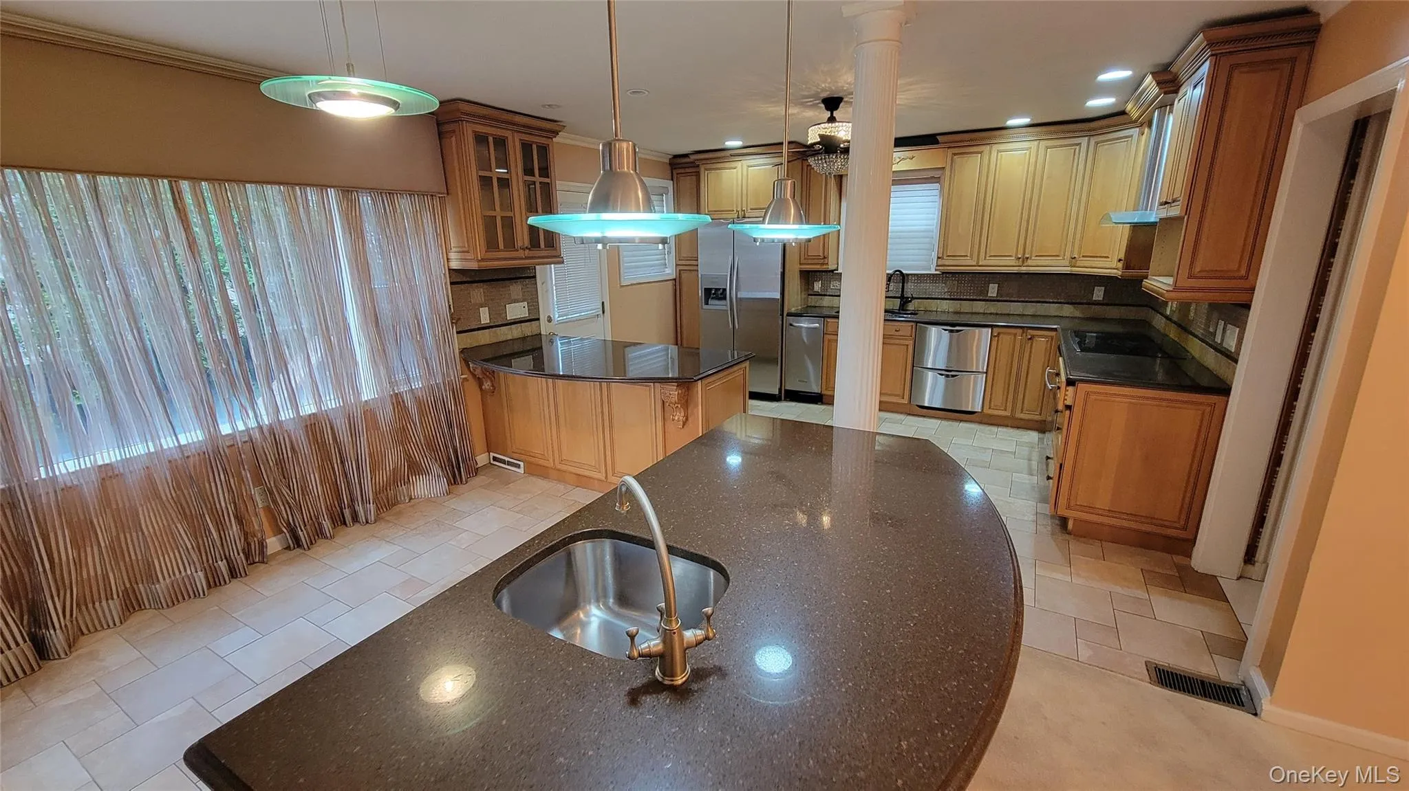 Kitchen with dark stone countertops, backsplash, glass insert cabinets, brown cabinetry, and recessed lighting Kitchen with dark stone countertops, backsplash, glass insert cabinets, brown cabinetry, and recessed lighting