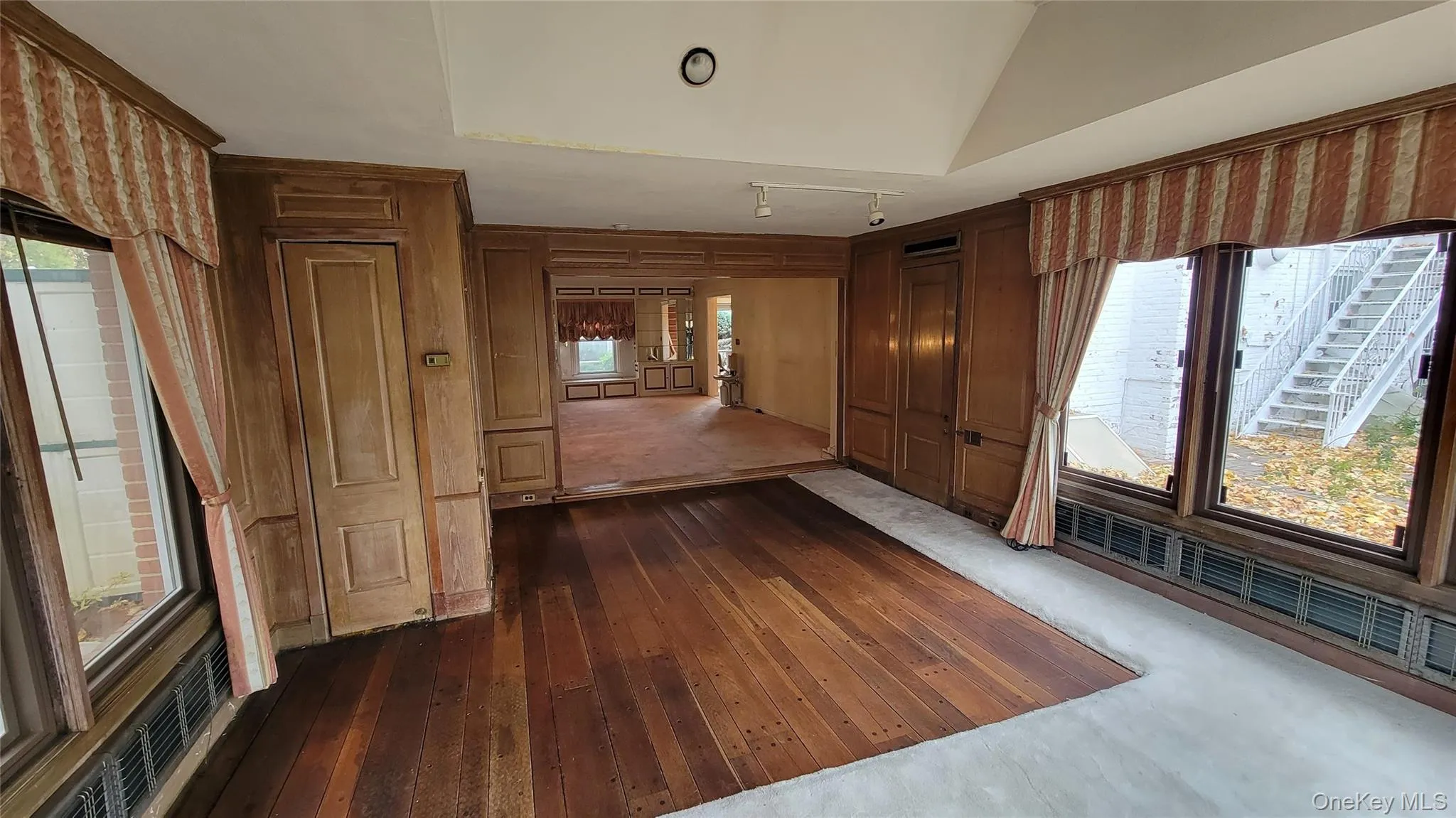 Unfurnished room featuring plenty of natural light, dark wood finished floors, and vaulted ceiling Unfurnished room featuring plenty of natural light, dark wood finished floors, and vaulted ceiling