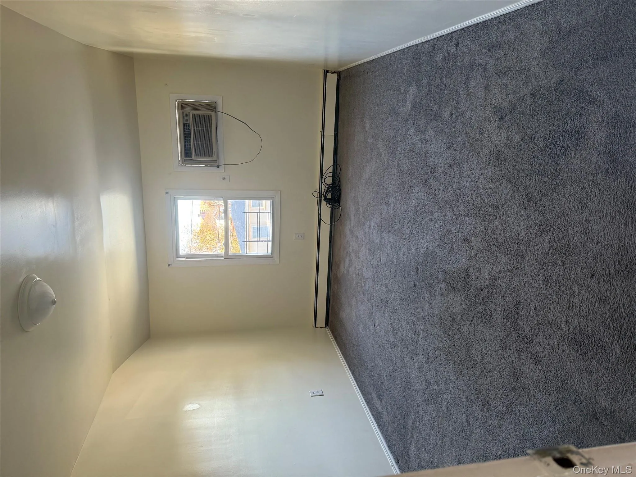 Unfurnished room featuring dark colored carpet, a wall mounted air conditioner, and baseboard heating Unfurnished room featuring dark colored carpet, a wall mounted air conditioner, and baseboard heating