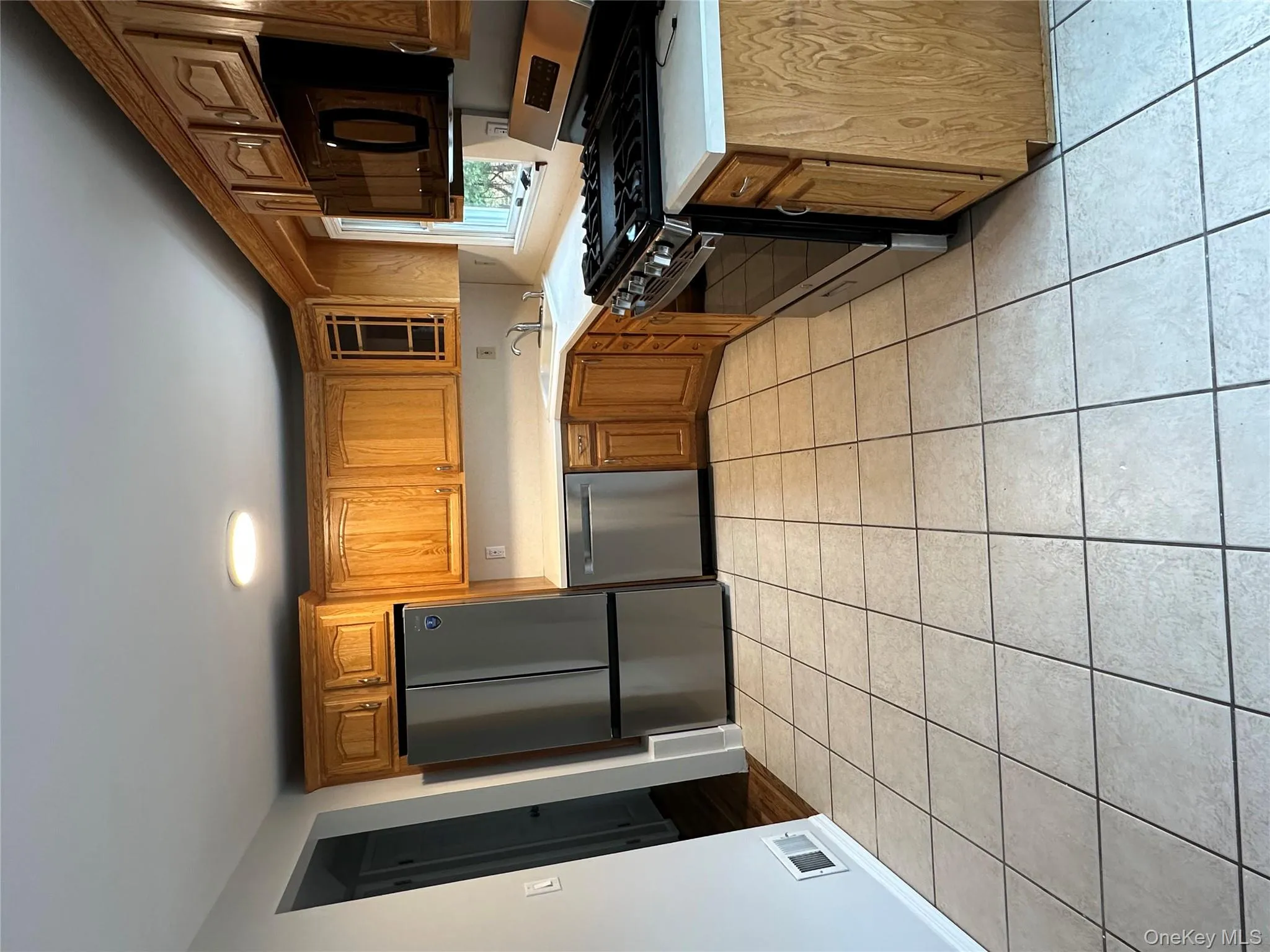 Kitchen with stainless steel appliances, light countertops, light tile patterned floors, and brown cabinets Kitchen with stainless steel appliances, light countertops, light tile patterned floors, and brown cabinets