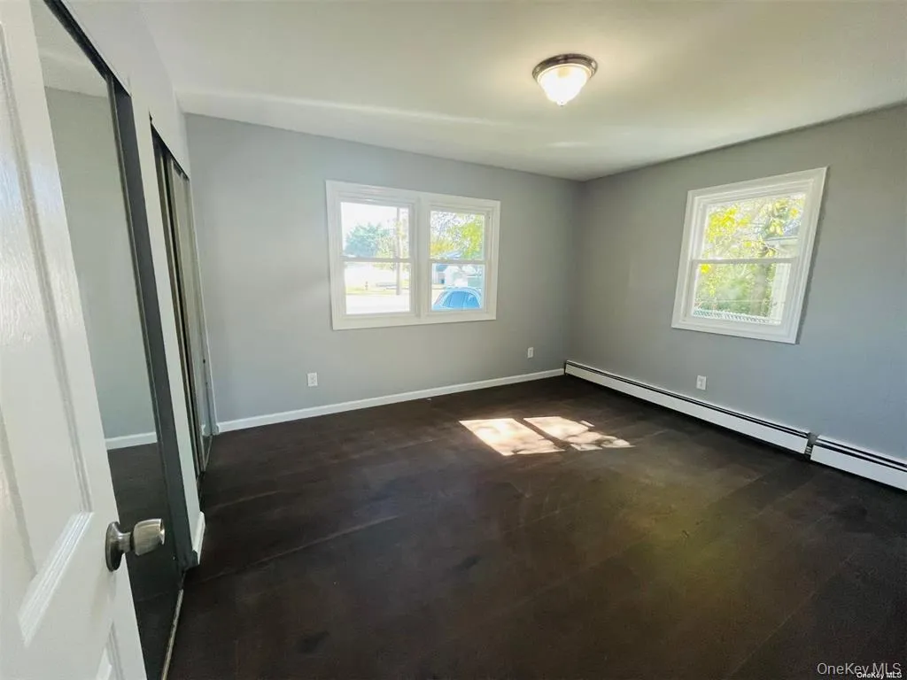 Unfurnished bedroom featuring dark wood-style floors, a closet, and baseboard heating Unfurnished bedroom featuring dark wood-style floors, a closet, and baseboard heating