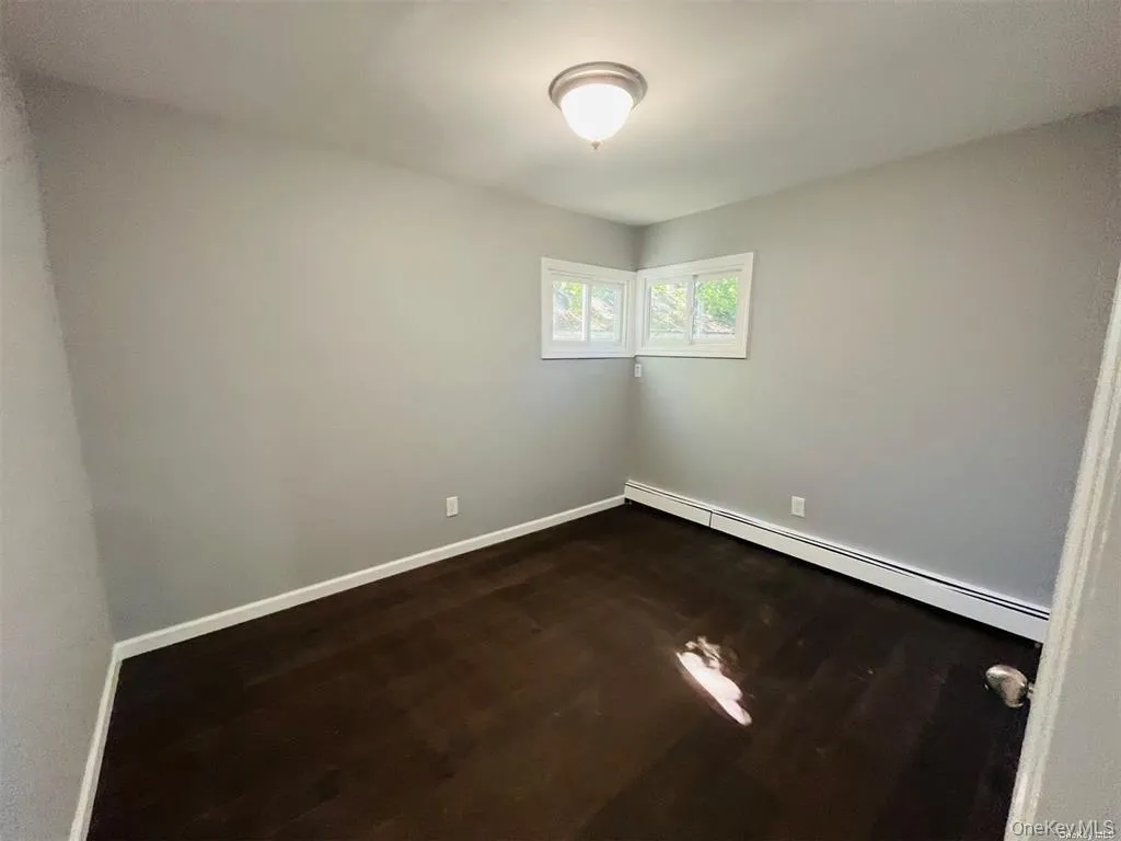 Empty room with a baseboard heating unit and dark wood-style floors Empty room with a baseboard heating unit and dark wood-style floors