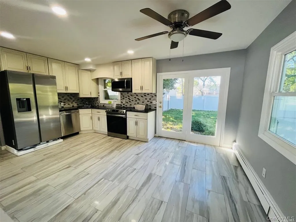 Kitchen with decorative backsplash, a baseboard radiator, appliances with stainless steel finishes, dark countertops, and recessed lighting Kitchen with decorative backsplash, a baseboard radiator, appliances with stainless steel finishes, dark countertops, and recessed lighting