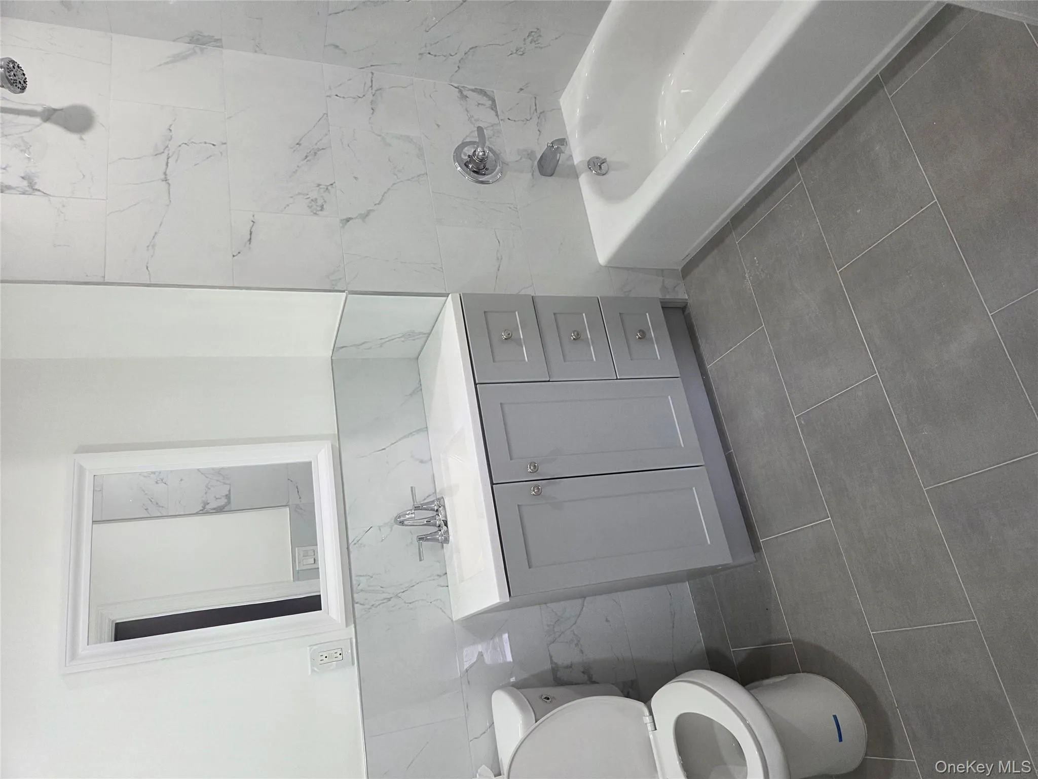 Bathroom featuring bathtub / shower combination, vanity, tile walls, and dark tile patterned floors Bathroom featuring bathtub / shower combination, vanity, tile walls, and dark tile patterned floors