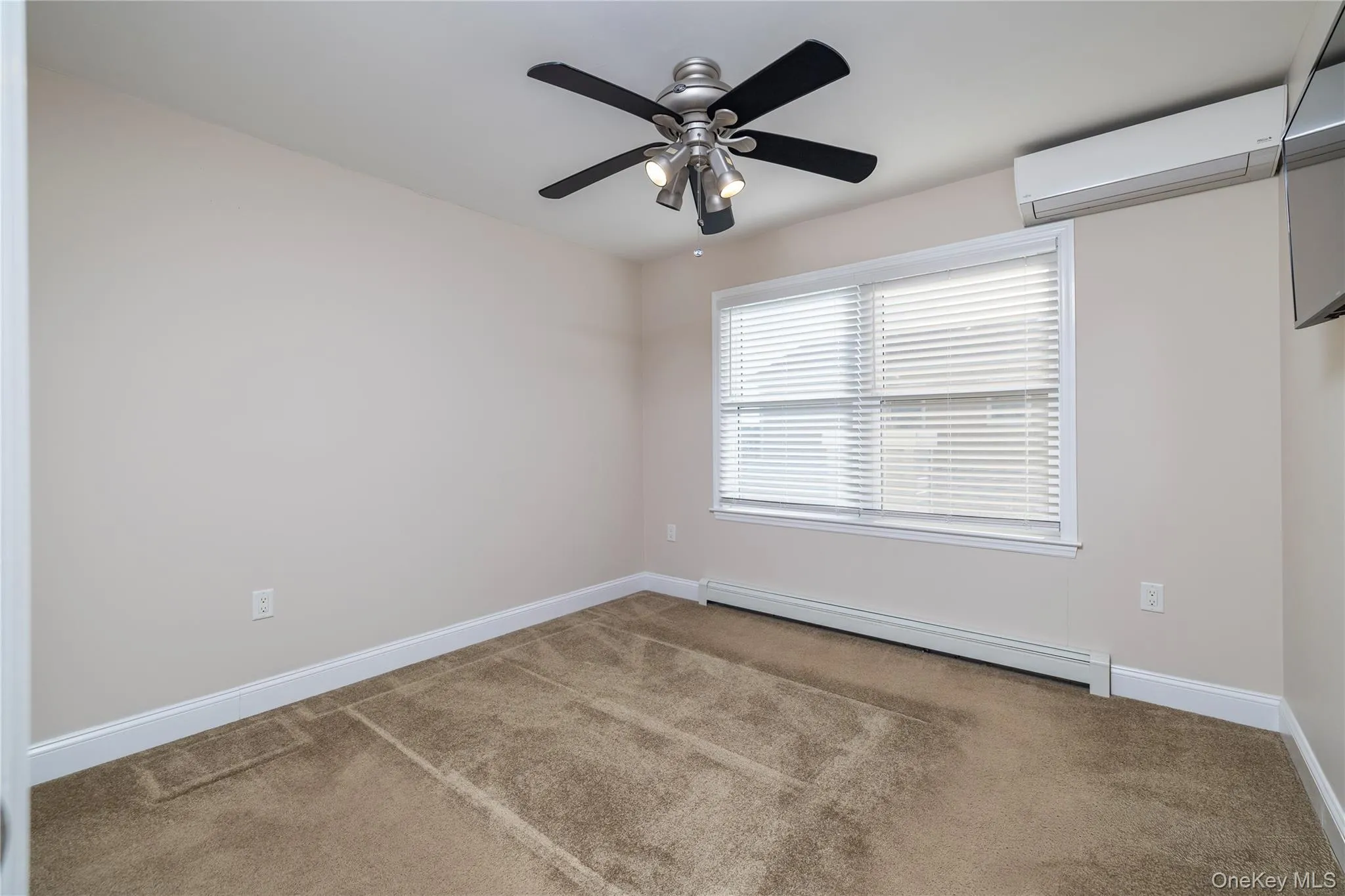 Spare room with a baseboard radiator, carpet, a ceiling fan, and an AC wall unit Spare room with a baseboard radiator, carpet, a ceiling fan, and an AC wall unit