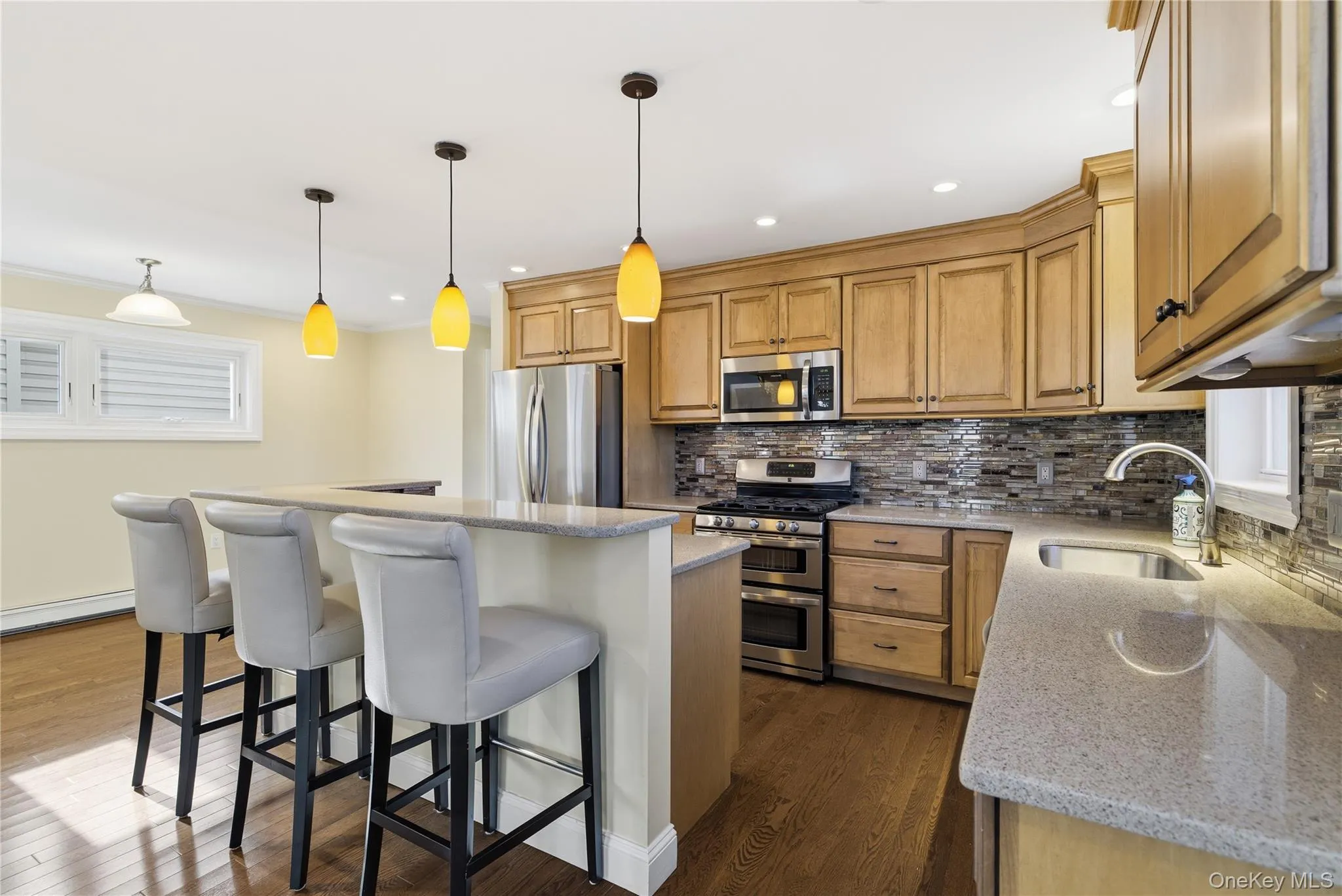 Kitchen featuring backsplash, appliances with stainless steel finishes, a center island, decorative light fixtures, and a kitchen bar Kitchen featuring backsplash, appliances with stainless steel finishes, a center island, decorative light fixtures, and a kitchen bar