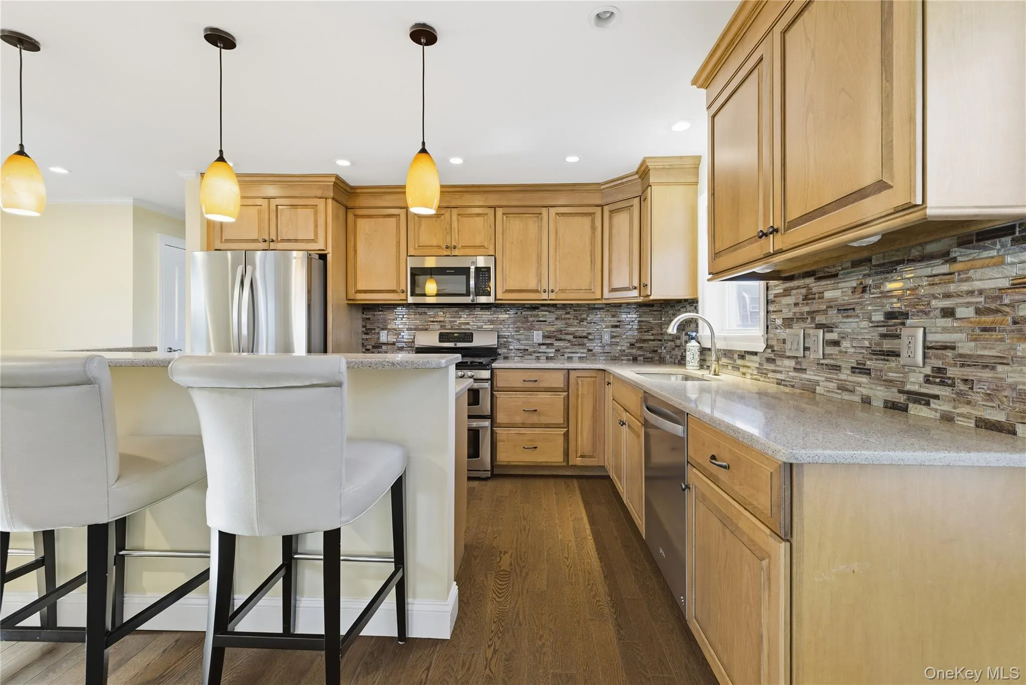 Kitchen with a breakfast bar, backsplash, appliances with stainless steel finishes, light stone countertops, and recessed lighting Kitchen with a breakfast bar, backsplash, appliances with stainless steel finishes, light stone countertops, and recessed lighting