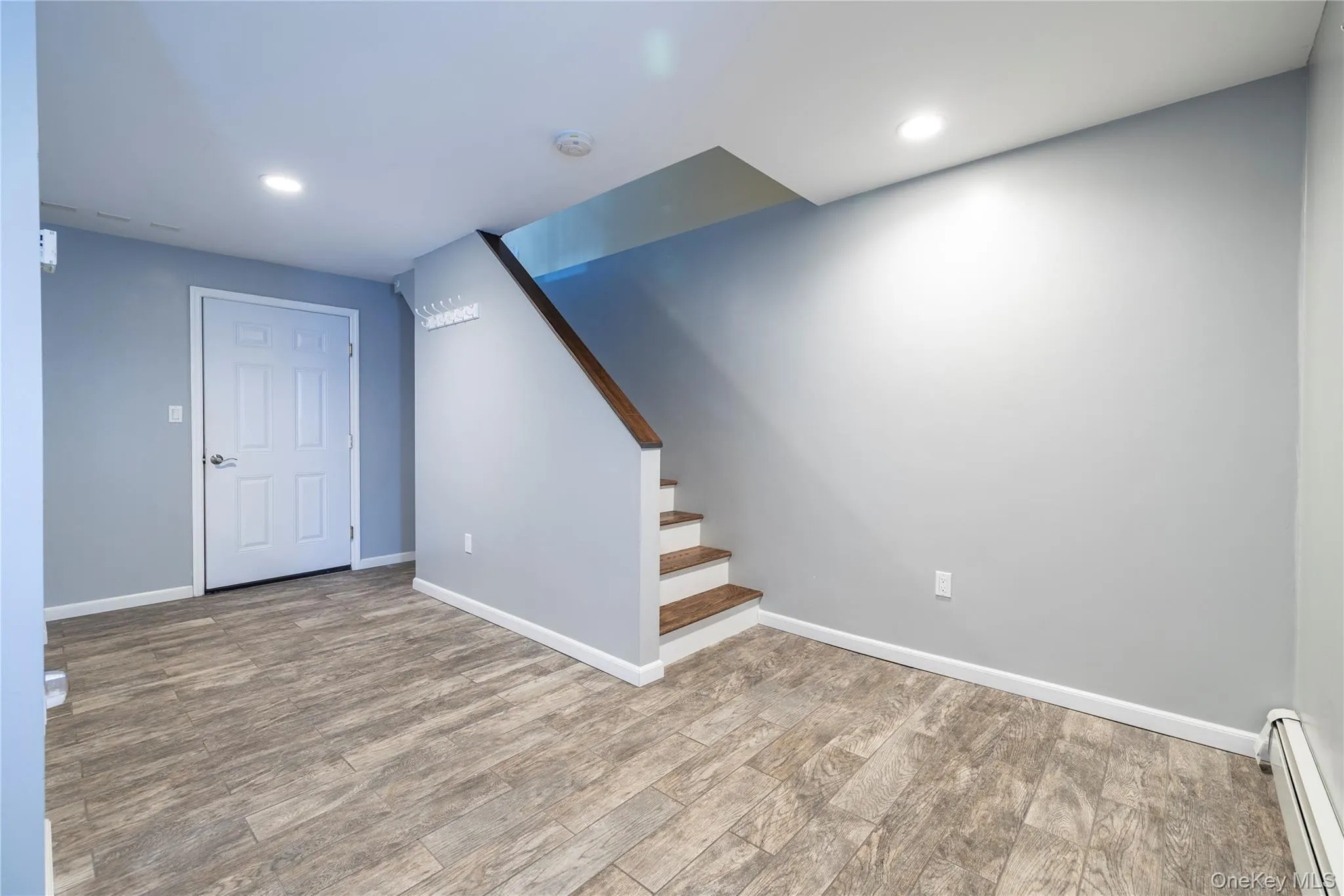 Finished below grade area featuring baseboard heating, wood finished floors, recessed lighting, and stairs Finished below grade area featuring baseboard heating, wood finished floors, recessed lighting, and stairs
