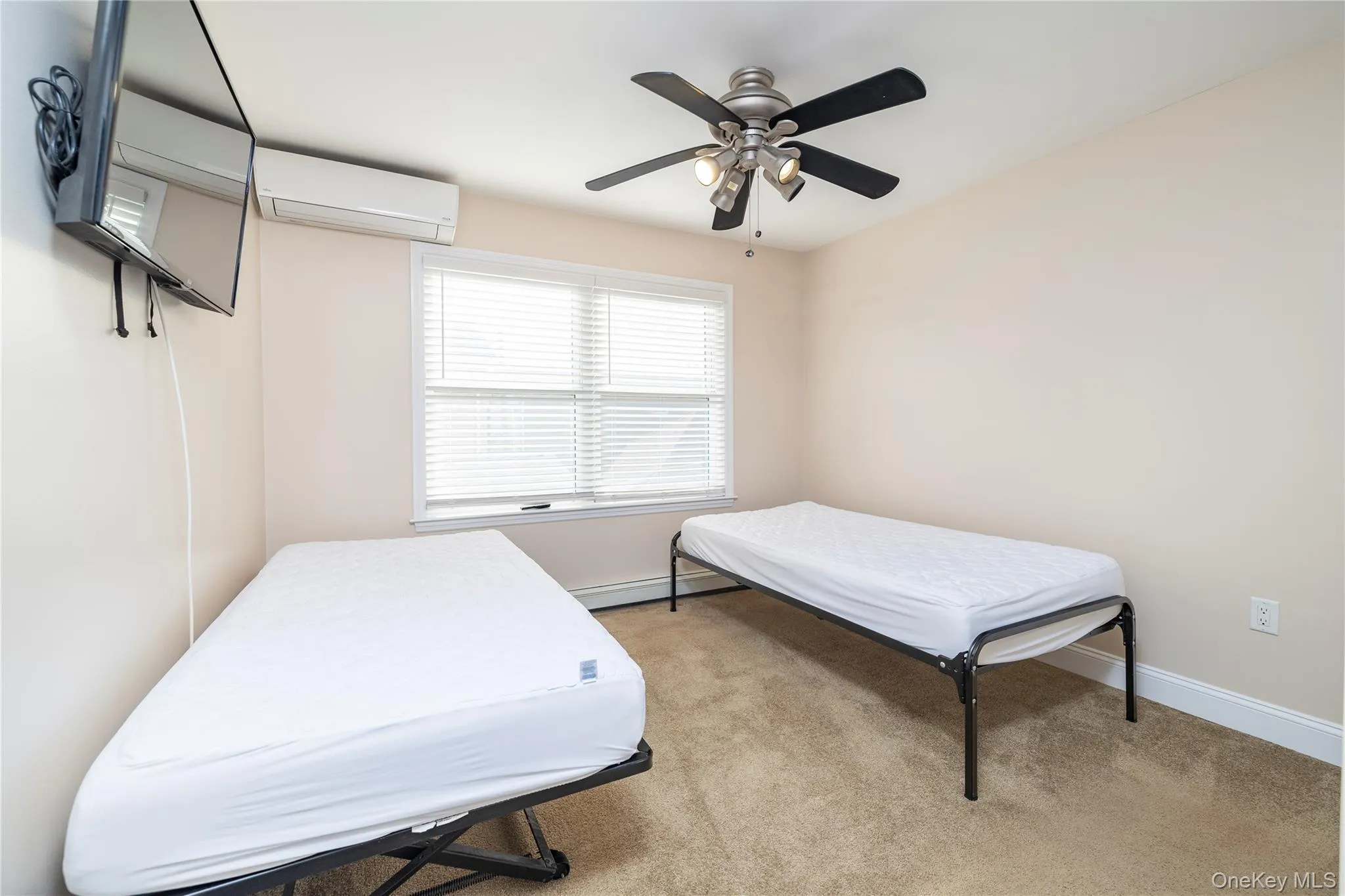 Bedroom featuring light carpet, ceiling fan, a wall unit AC, and a baseboard heating unit Bedroom featuring light carpet, ceiling fan, a wall unit AC, and a baseboard heating unit