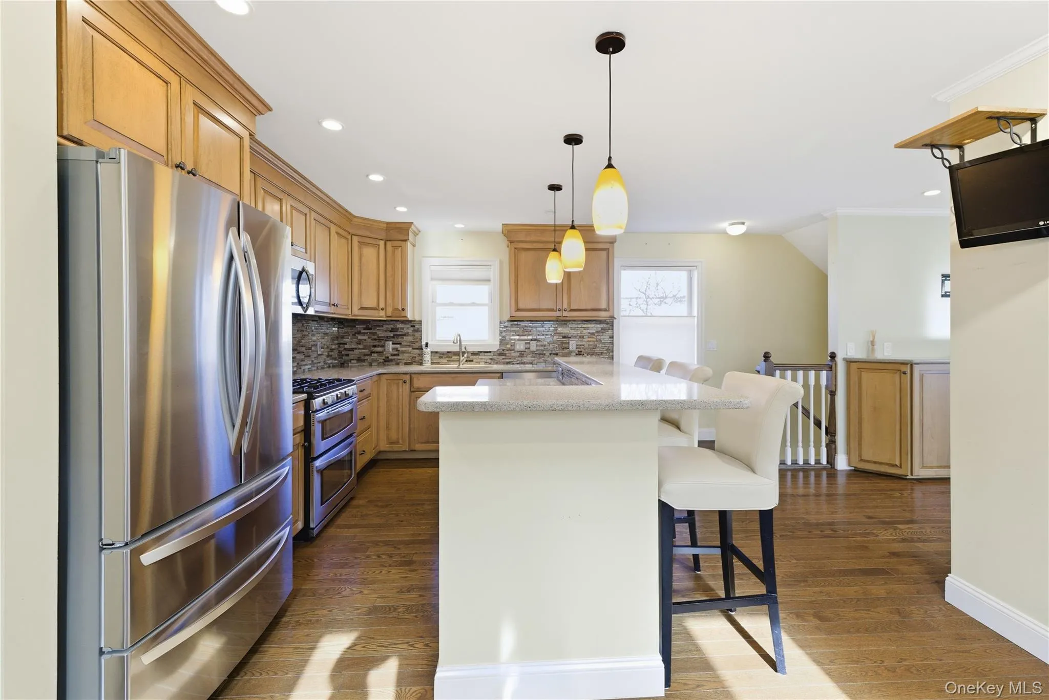 Kitchen with stainless steel appliances, a kitchen breakfast bar, dark wood finished floors, light stone countertops, and backsplash Kitchen with stainless steel appliances, a kitchen breakfast bar, dark wood finished floors, light stone countertops, and backsplash