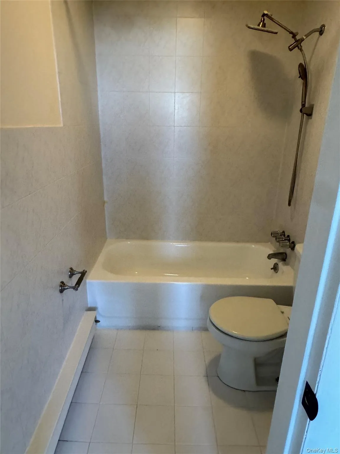 Bathroom featuring tile patterned floors, shower / bath combination, tile walls, and a baseboard heating unit Bathroom featuring tile patterned floors, shower / bath combination, tile walls, and a baseboard heating unit