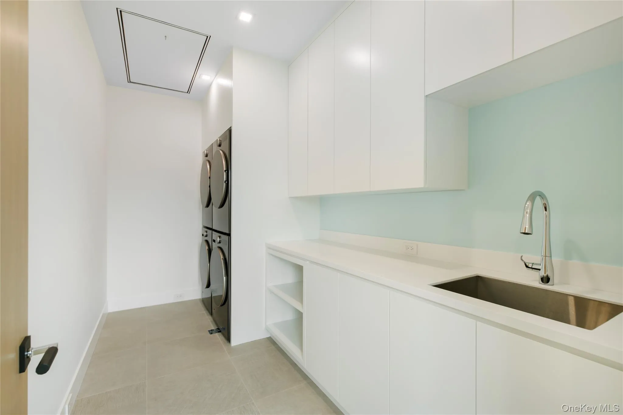 Laundry area featuring stacked washer / dryer, attic access, light tile patterned floors, and recessed lighting Laundry area featuring stacked washer / dryer, attic access, light tile patterned floors, and recessed lighting