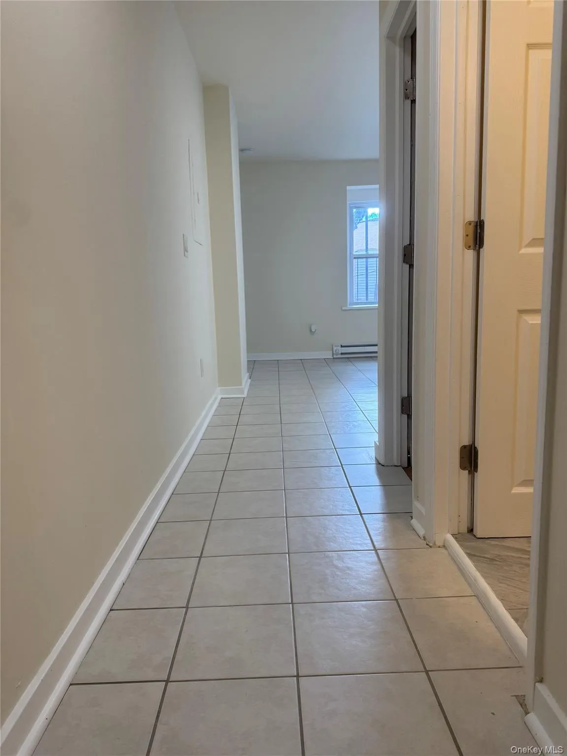 Hallway with light tile patterned floors and a baseboard radiator Hallway with light tile patterned floors and a baseboard radiator