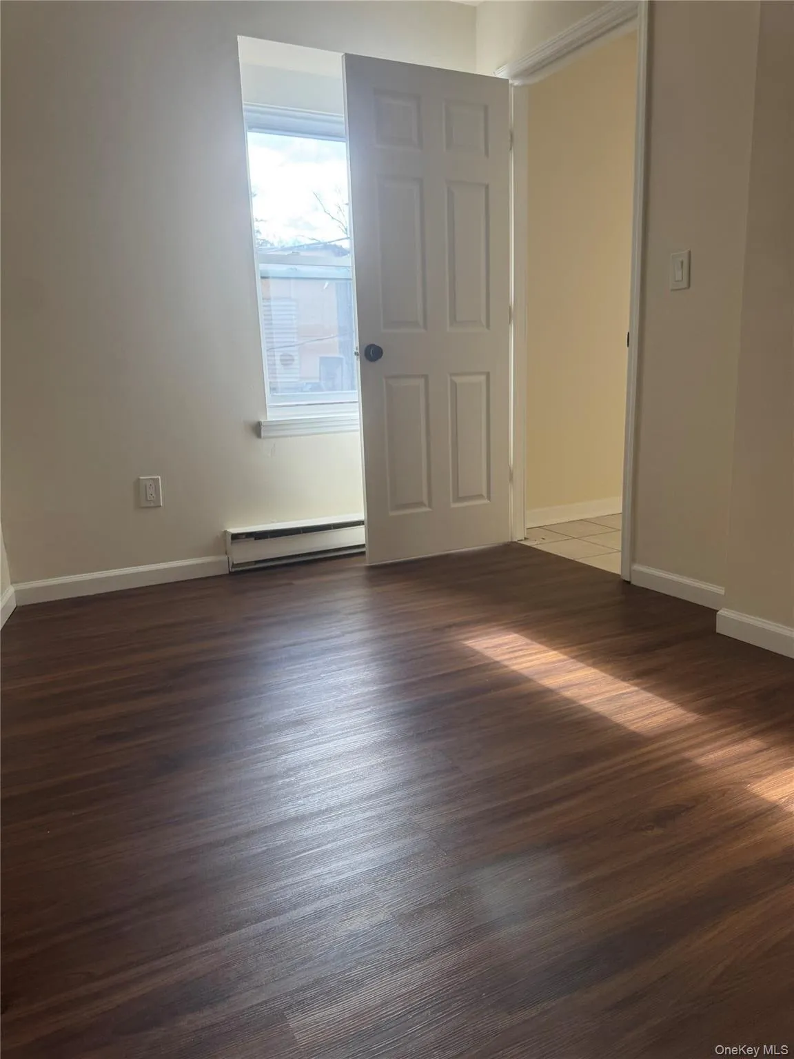 Spare room with a baseboard heating unit and dark wood-type flooring Spare room with a baseboard heating unit and dark wood-type flooring