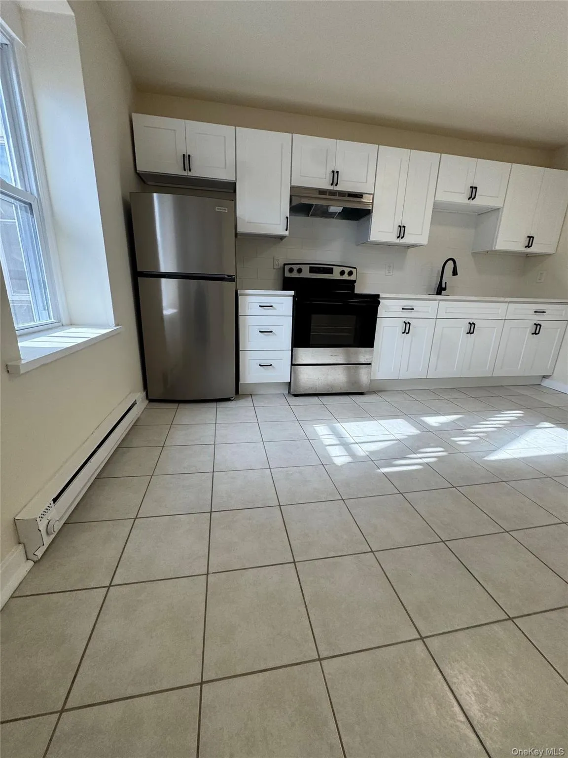 Kitchen featuring baseboard heating, white cabinets, appliances with stainless steel finishes, and light tile patterned floors Kitchen featuring baseboard heating, white cabinets, appliances with stainless steel finishes, and light tile patterned floors