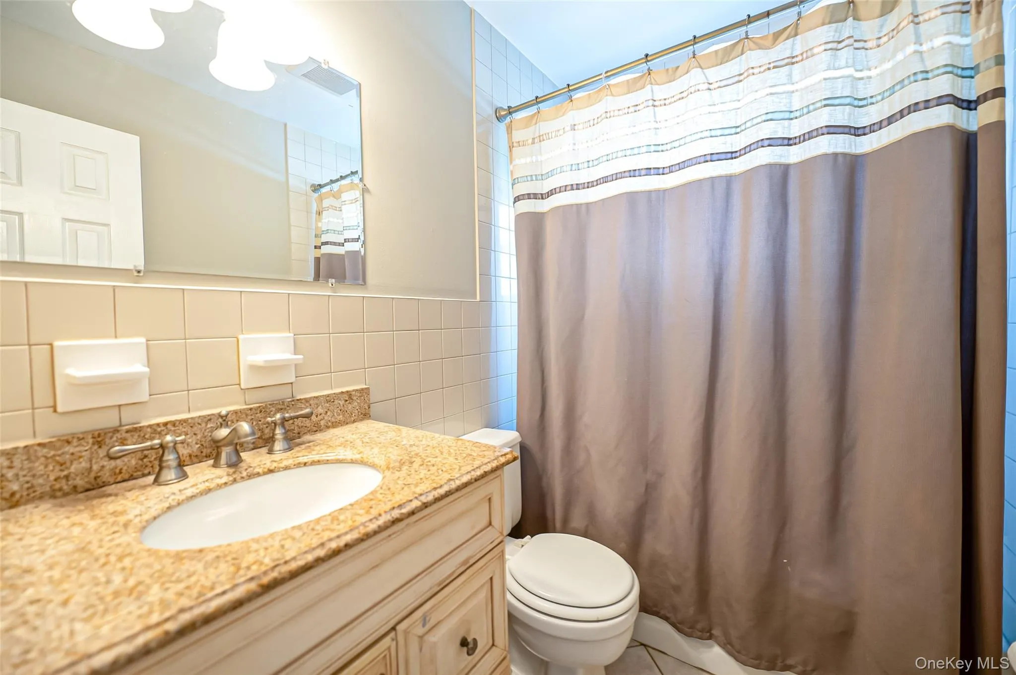 Bathroom featuring vanity, toilet, and tile walls Bathroom featuring vanity, toilet, and tile walls