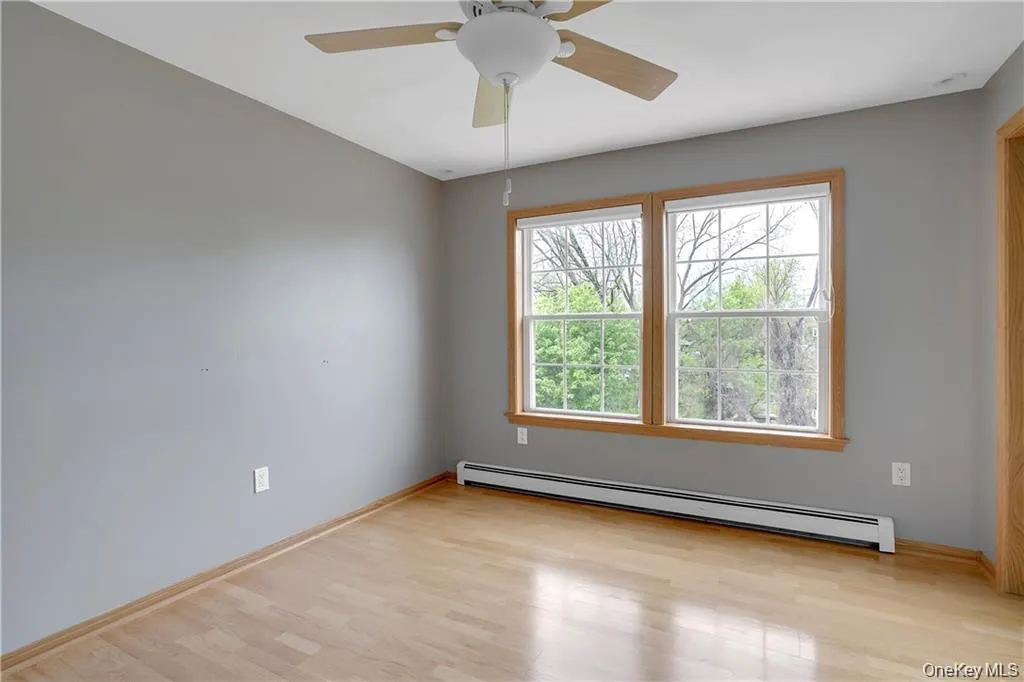 Empty room with baseboard heating, light wood-style floors, and ceiling fan Empty room with baseboard heating, light wood-style floors, and ceiling fan