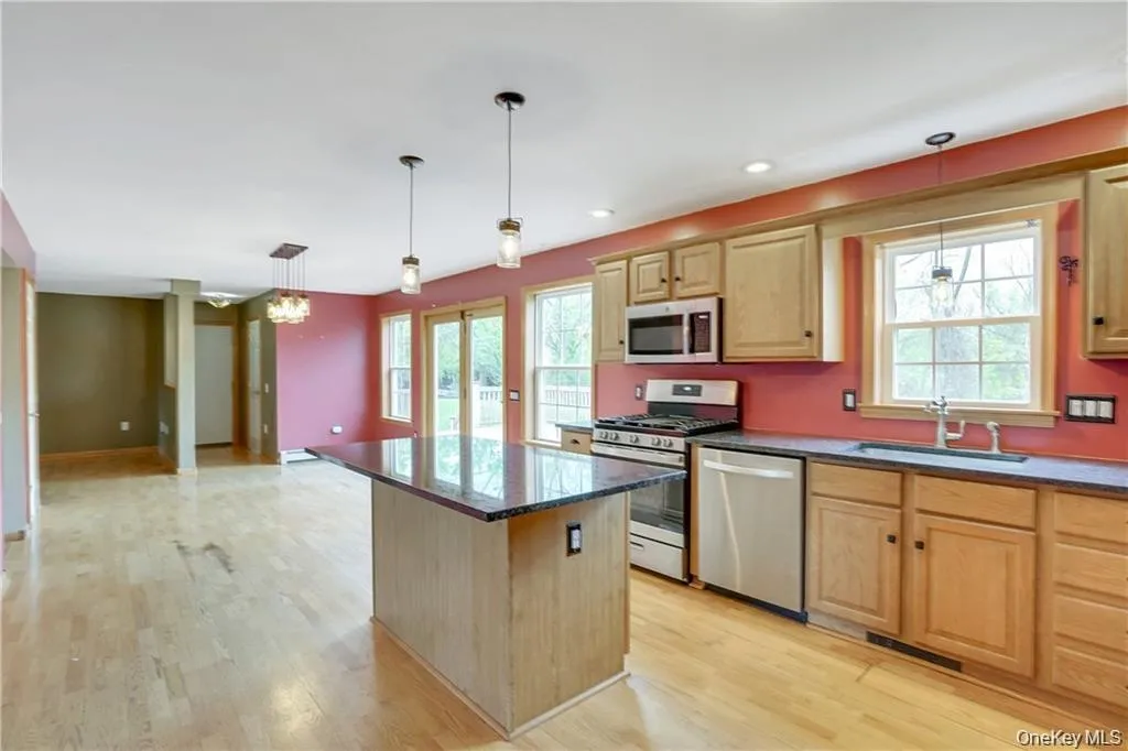 Kitchen with appliances with stainless steel finishes, a kitchen island, pendant lighting, open floor plan, and light wood-style floors Kitchen with appliances with stainless steel finishes, a kitchen island, pendant lighting, open floor plan, and light wood-style floors