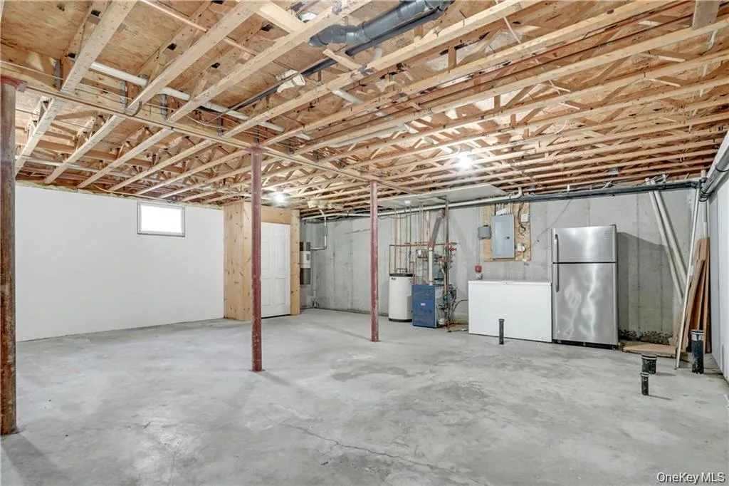 Below grade area featuring freestanding refrigerator, water heater, and electric panel Below grade area featuring freestanding refrigerator, water heater, and electric panel