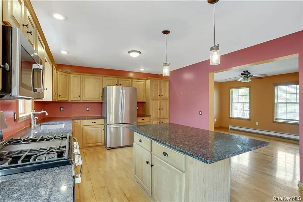 Kitchen with appliances with stainless steel finishes, light wood-style flooring, a center island, baseboard heating, and decorative light fixtures Kitchen with appliances with stainless steel finishes, light wood-style flooring, a center island, baseboard heating, and decorative light fixtures