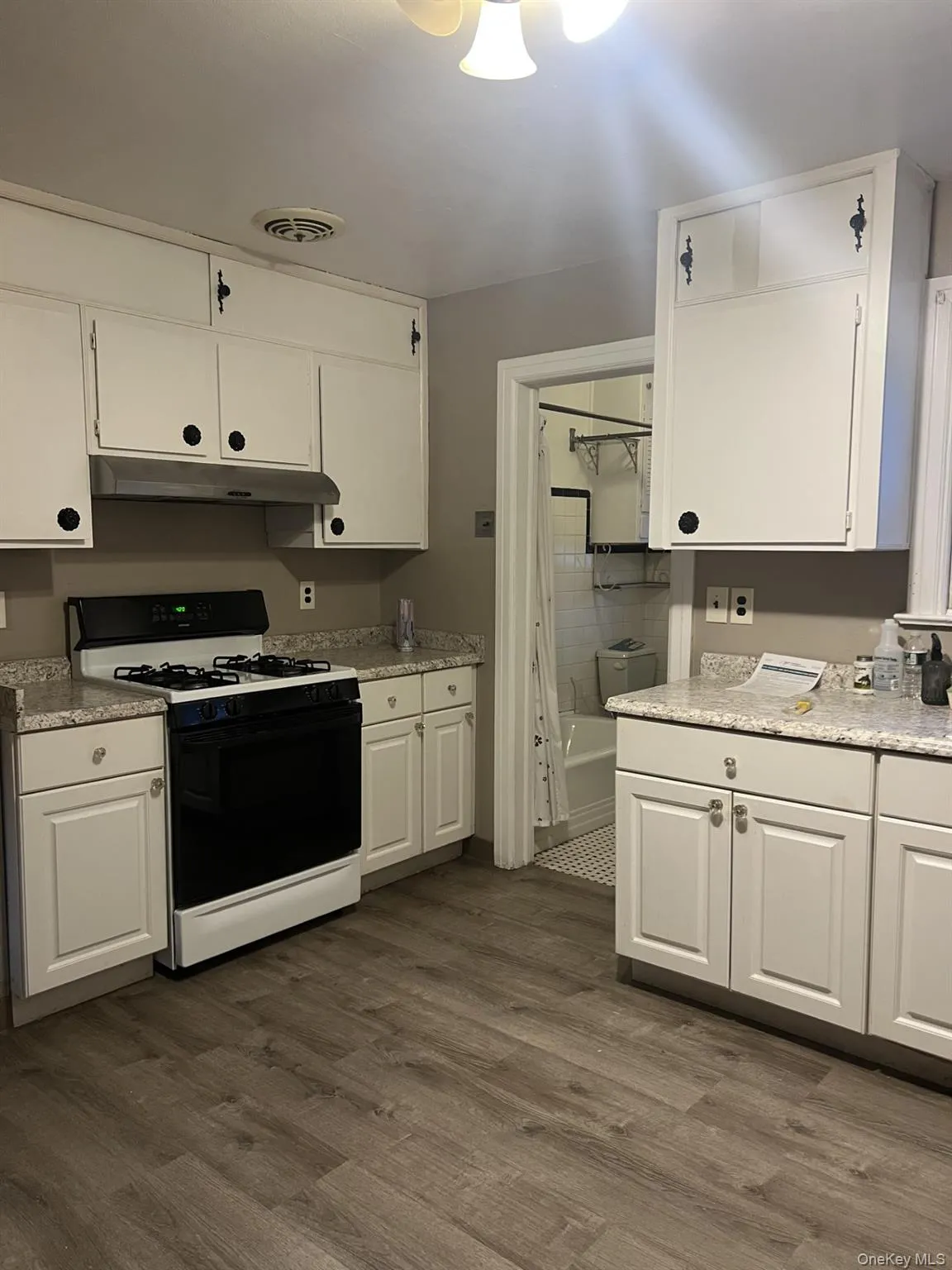 Kitchen with range with gas cooktop, white cabinets, dark wood-style flooring, under cabinet range hood, and light stone countertops Kitchen with range with gas cooktop, white cabinets, dark wood-style flooring, under cabinet range hood, and light stone countertops