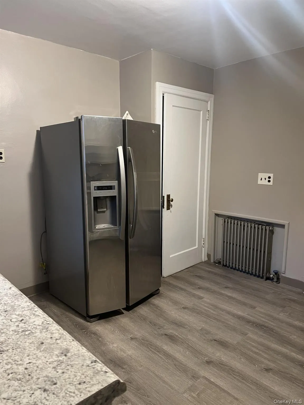 Kitchen with stainless steel fridge with ice dispenser, light wood-style floors, and radiator heating unit Kitchen with stainless steel fridge with ice dispenser, light wood-style floors, and radiator heating unit