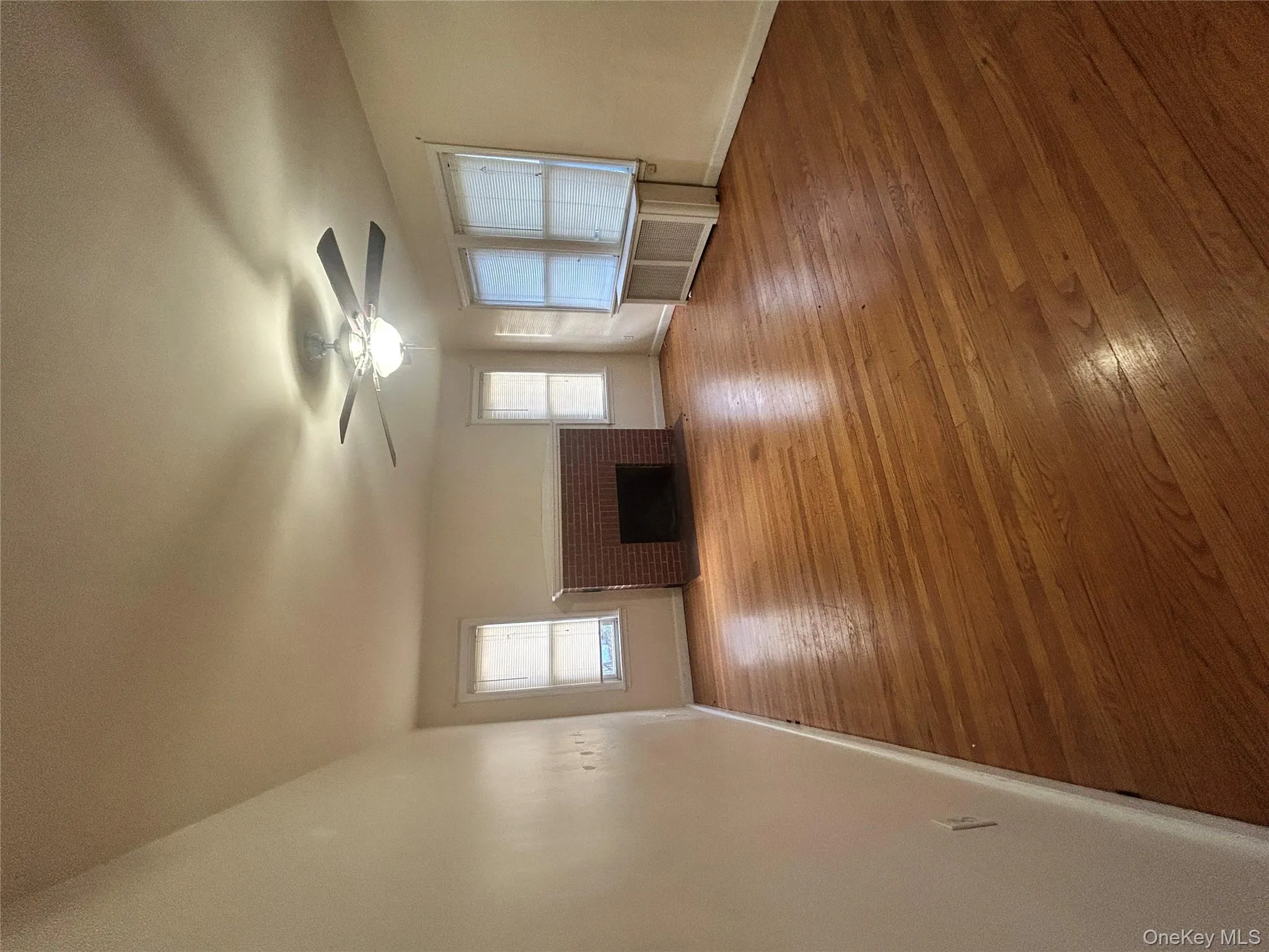Unfurnished living room featuring hardwood / wood-style floors, a brick fireplace, radiator, and a ceiling fan Unfurnished living room featuring hardwood / wood-style floors, a brick fireplace, radiator, and a ceiling fan