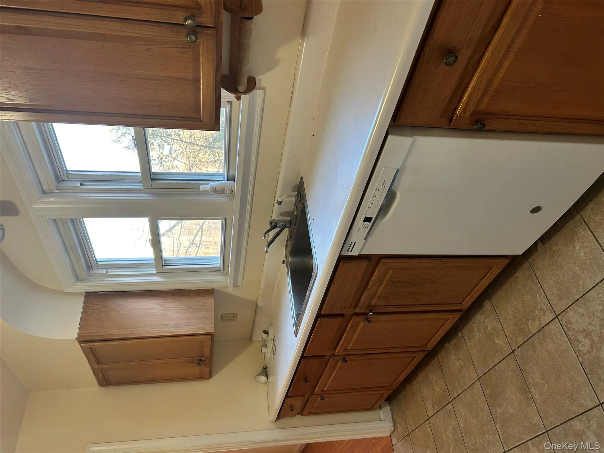 Kitchen featuring brown cabinetry, dishwashing machine, light countertops, and light tile patterned flooring Kitchen featuring brown cabinetry, dishwashing machine, light countertops, and light tile patterned flooring