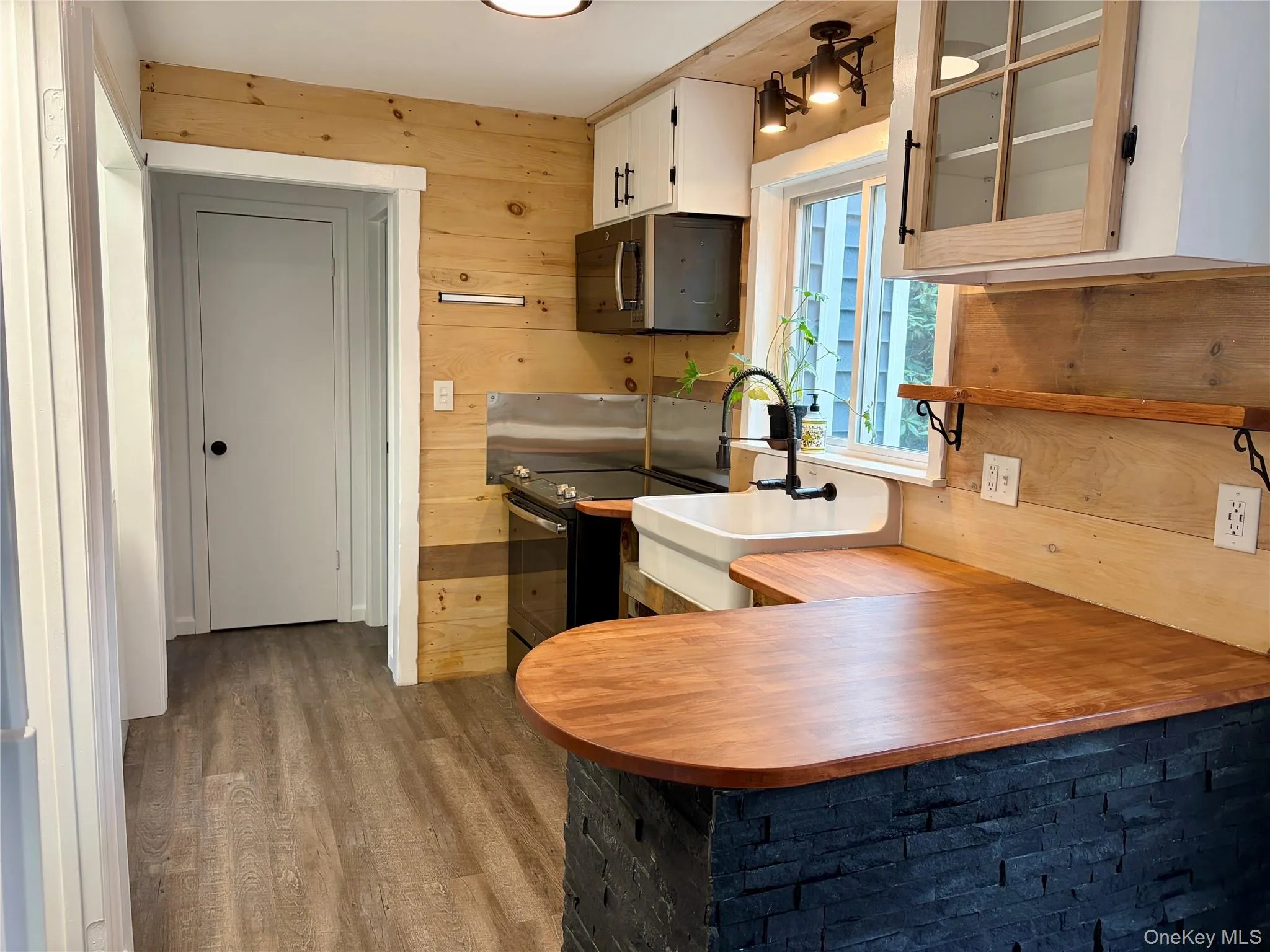 Kitchen featuring wooden walls, black appliances, dark wood-style flooring, glass insert cabinets, and a peninsula Kitchen featuring wooden walls, black appliances, dark wood-style flooring, glass insert cabinets, and a peninsula