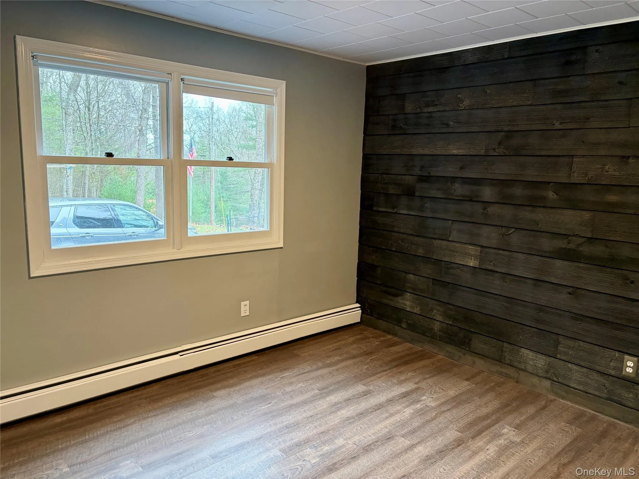 Unfurnished room with baseboard heating, wood walls, and wood finished floors Unfurnished room with baseboard heating, wood walls, and wood finished floors