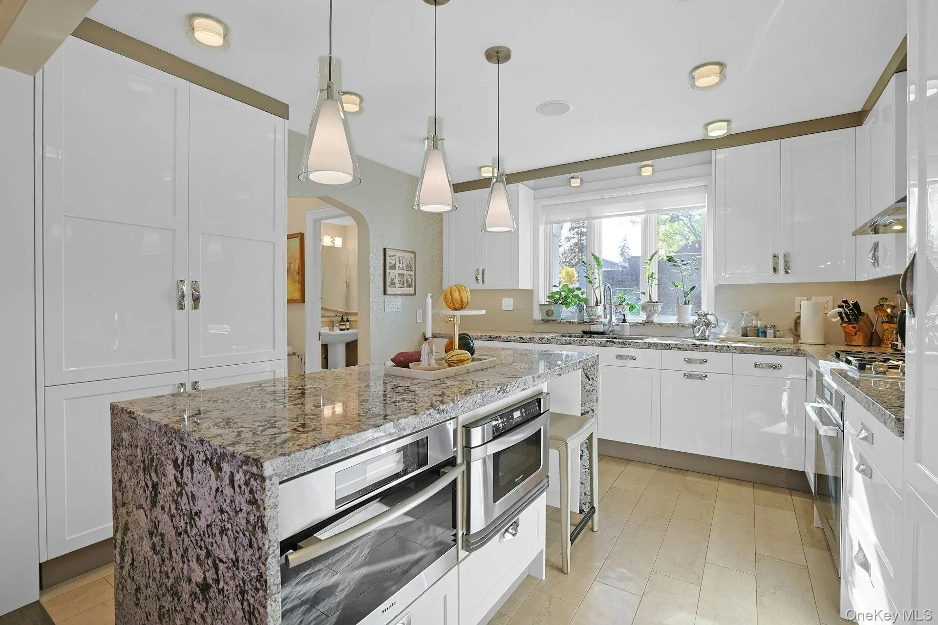 Kitchen featuring white cabinets, hanging light fixtures, arched walkways, and light stone counters Kitchen featuring white cabinets, hanging light fixtures, arched walkways, and light stone counters