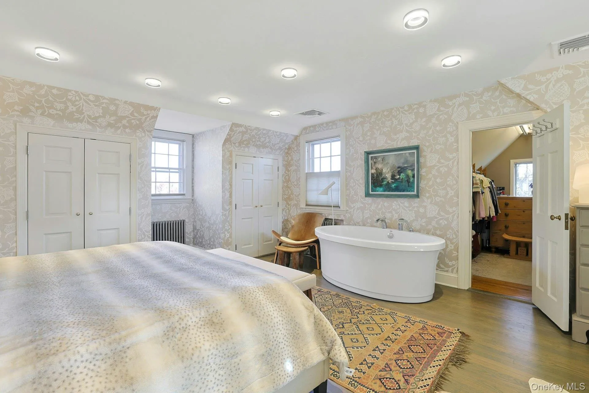 Bedroom featuring a closet, wallpapered walls, multiple windows, radiator, and wood finished floors Bedroom featuring a closet, wallpapered walls, multiple windows, radiator, and wood finished floors