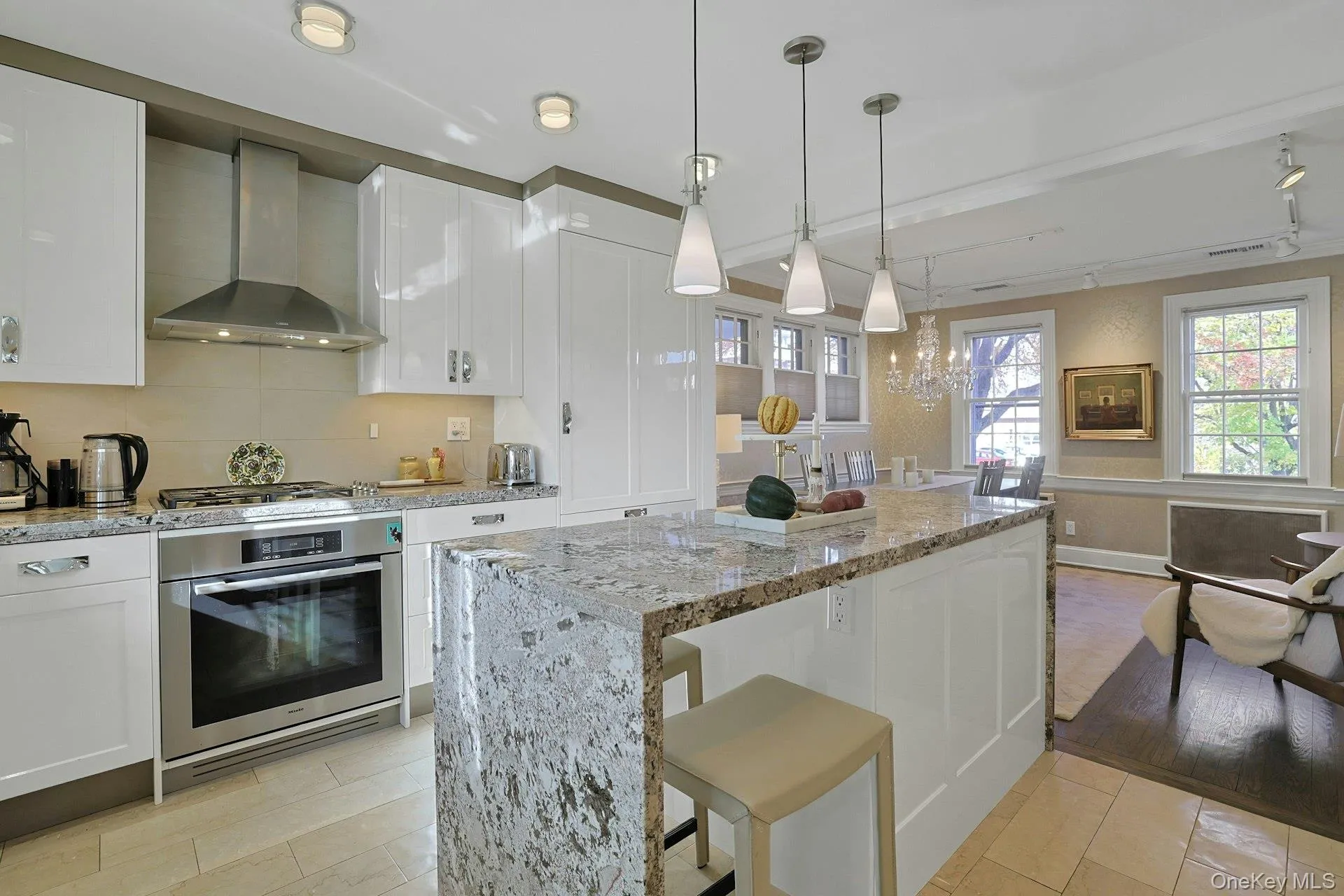 Kitchen featuring white cabinets, wall chimney range hood, and light stone counters Kitchen featuring white cabinets, wall chimney range hood, and light stone counters