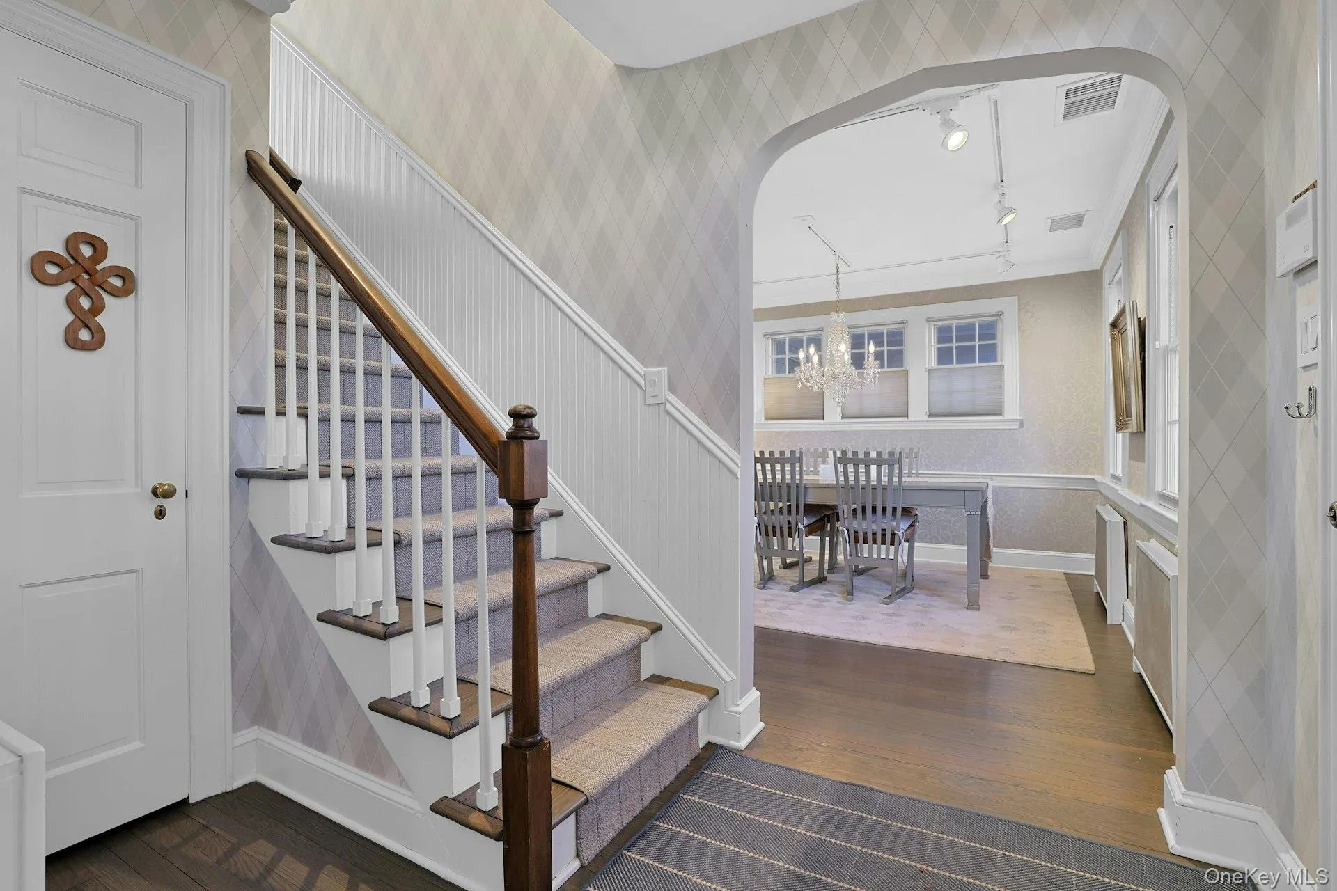 Stairway with wallpapered walls, wood finished floors, track lighting, arched walkways, and a chandelier Stairway with wallpapered walls, wood finished floors, track lighting, arched walkways, and a chandelier