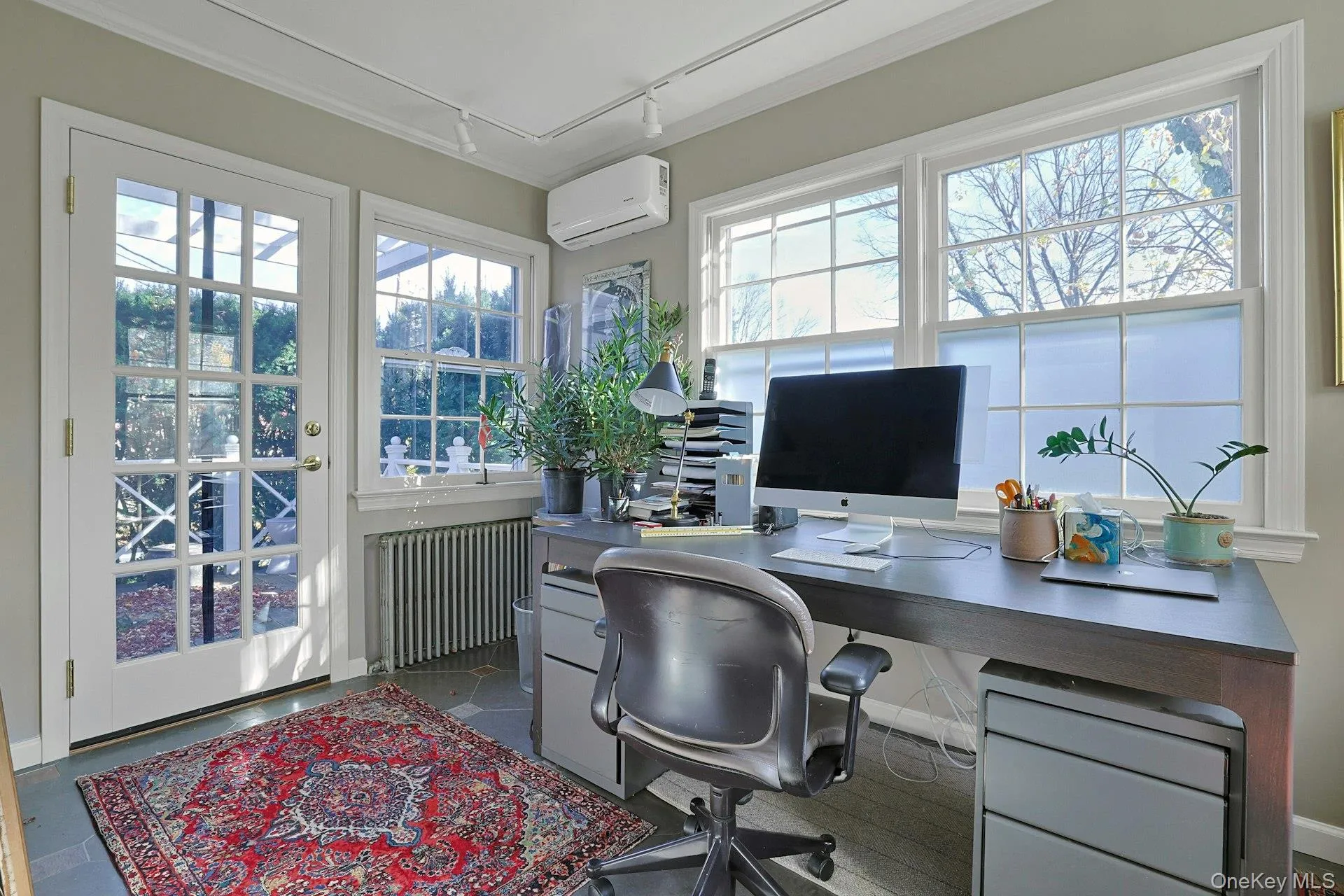 Office space featuring rail lighting, radiator, a wall mounted air conditioner, and plenty of natural light Office space featuring rail lighting, radiator, a wall mounted air conditioner, and plenty of natural light