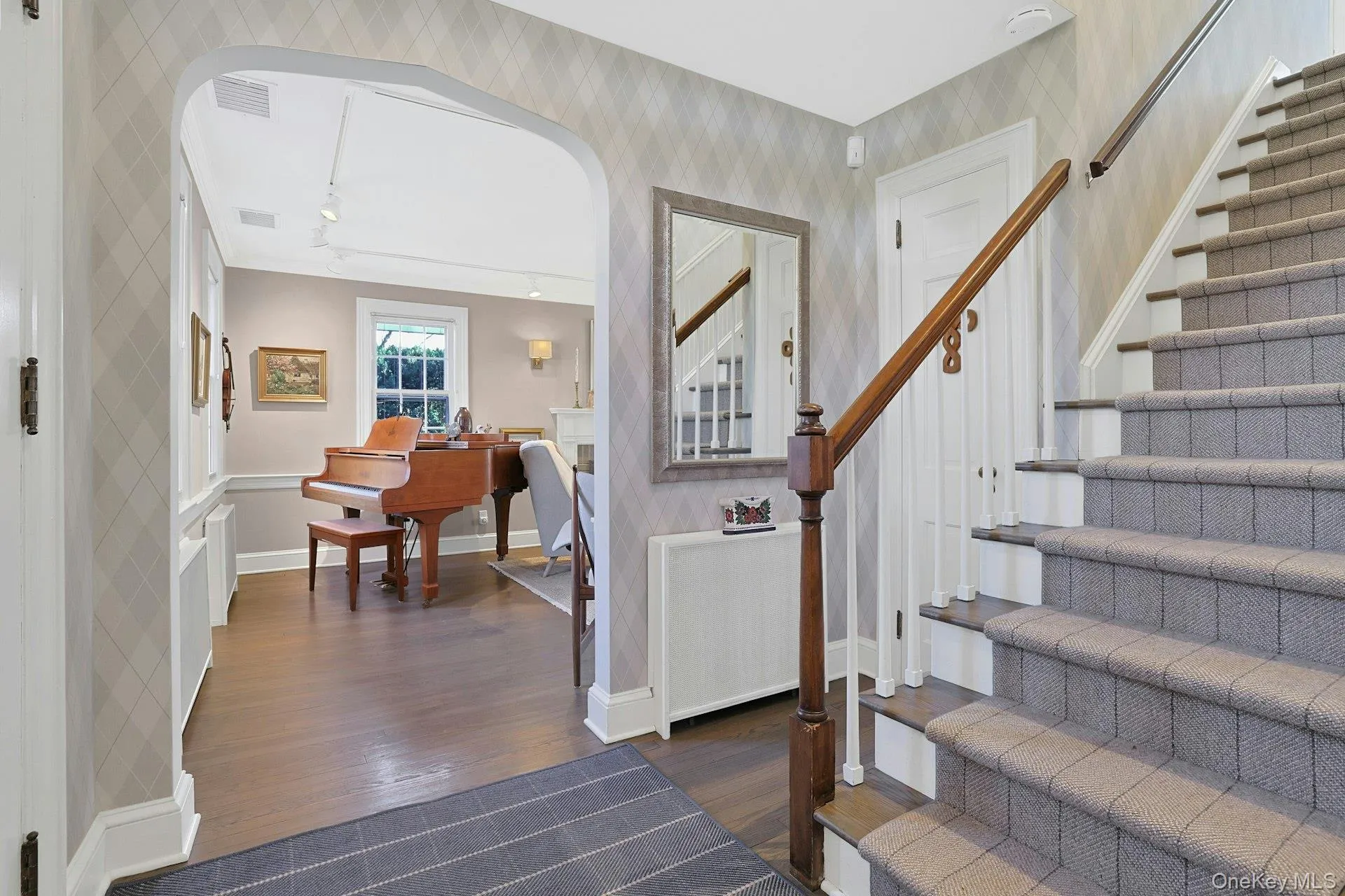 Staircase featuring arched walkways, wood finished floors, and wallpapered walls Staircase featuring arched walkways, wood finished floors, and wallpapered walls