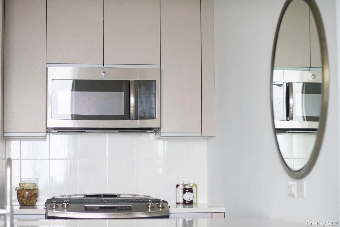 Kitchen with appliances with stainless steel finishes, decorative backsplash, light countertops, and gray cabinets Kitchen with appliances with stainless steel finishes, decorative backsplash, light countertops, and gray cabinets