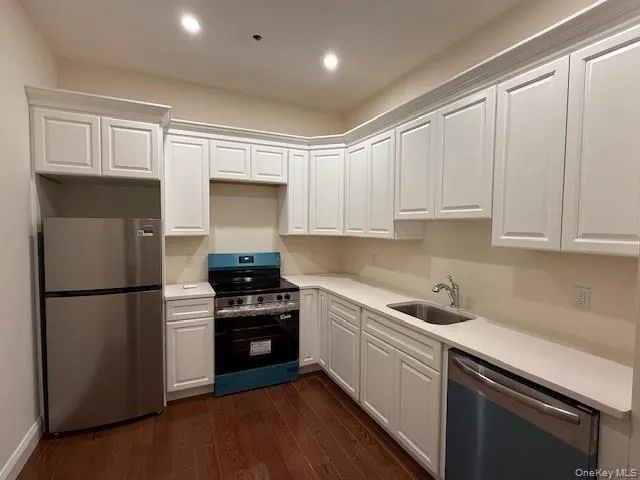 Kitchen with appliances with stainless steel finishes, white cabinetry, dark wood-type flooring, light stone counters, and recessed lighting Kitchen with appliances with stainless steel finishes, white cabinetry, dark wood-type flooring, light stone counters, and recessed lighting