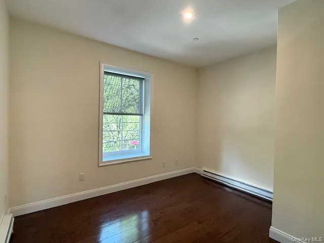 Empty room featuring dark wood-style flooring, a baseboard heating unit, and recessed lighting Empty room featuring dark wood-style flooring, a baseboard heating unit, and recessed lighting