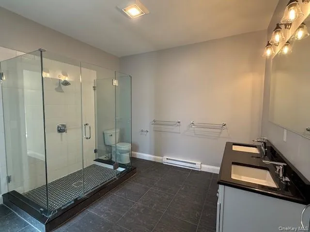 Bathroom featuring double vanity, a stall shower, and a baseboard radiator Bathroom featuring double vanity, a stall shower, and a baseboard radiator