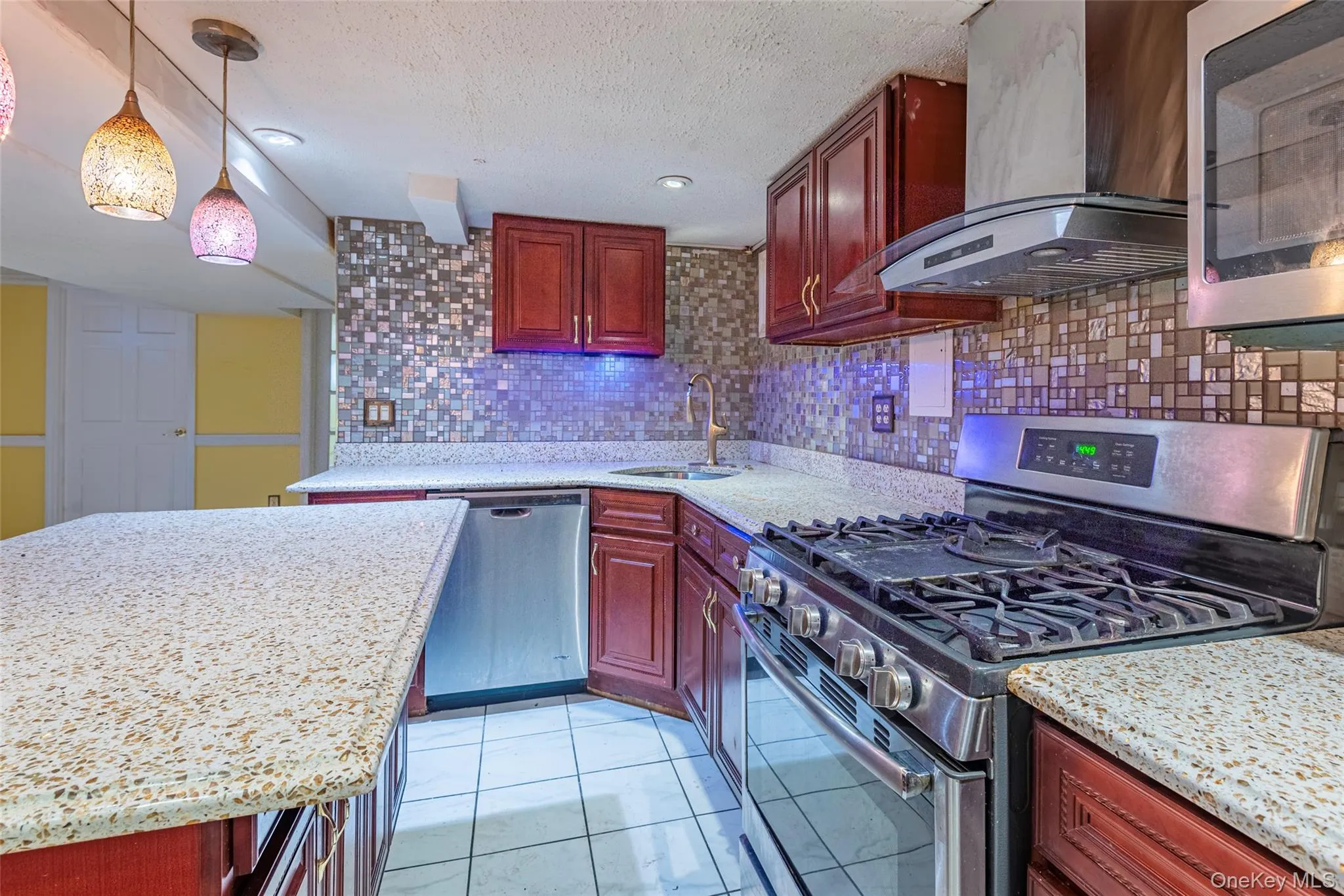 Kitchen with appliances with stainless steel finishes, exhaust hood, tasteful backsplash, dark brown cabinets, and decorative light fixtures Kitchen with appliances with stainless steel finishes, exhaust hood, tasteful backsplash, dark brown cabinets, and decorative light fixtures