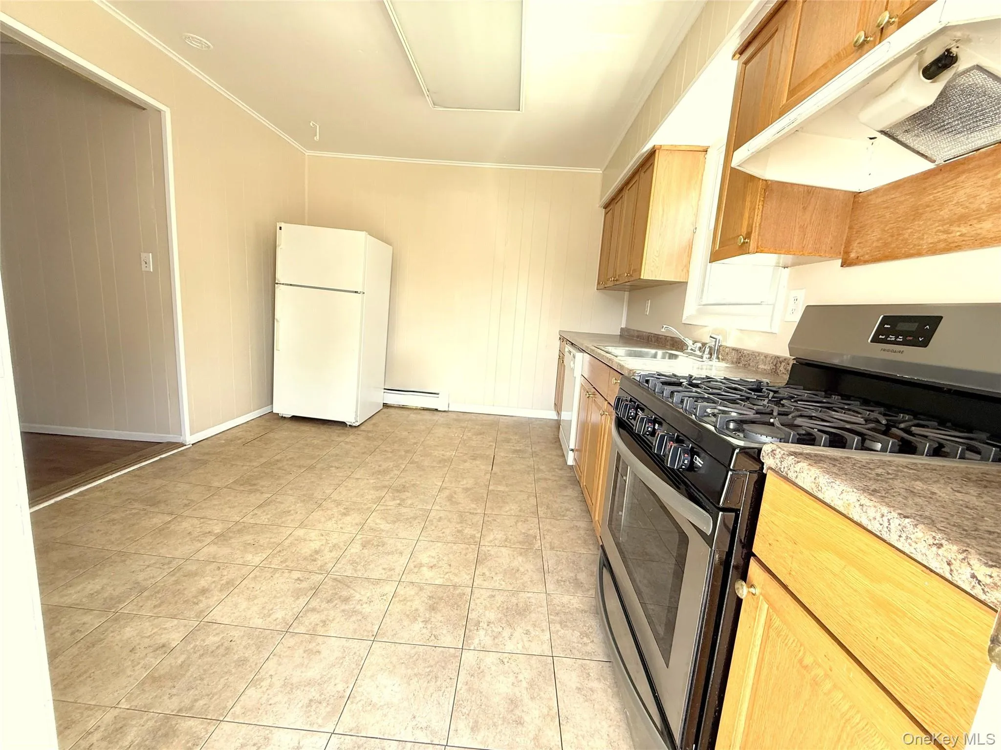 Kitchen with white appliances, under cabinet range hood, light countertops, crown molding, and a baseboard heating unit Kitchen with white appliances, under cabinet range hood, light countertops, crown molding, and a baseboard heating unit
