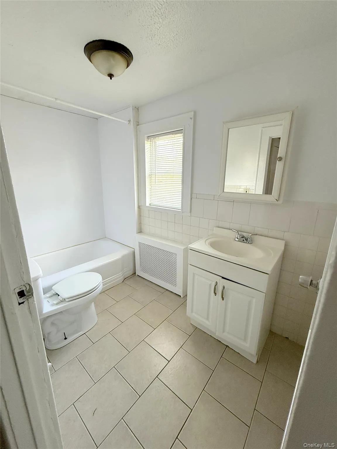 Bathroom with radiator, vanity, tile walls, tile patterned flooring, and a textured ceiling Bathroom with radiator, vanity, tile walls, tile patterned flooring, and a textured ceiling