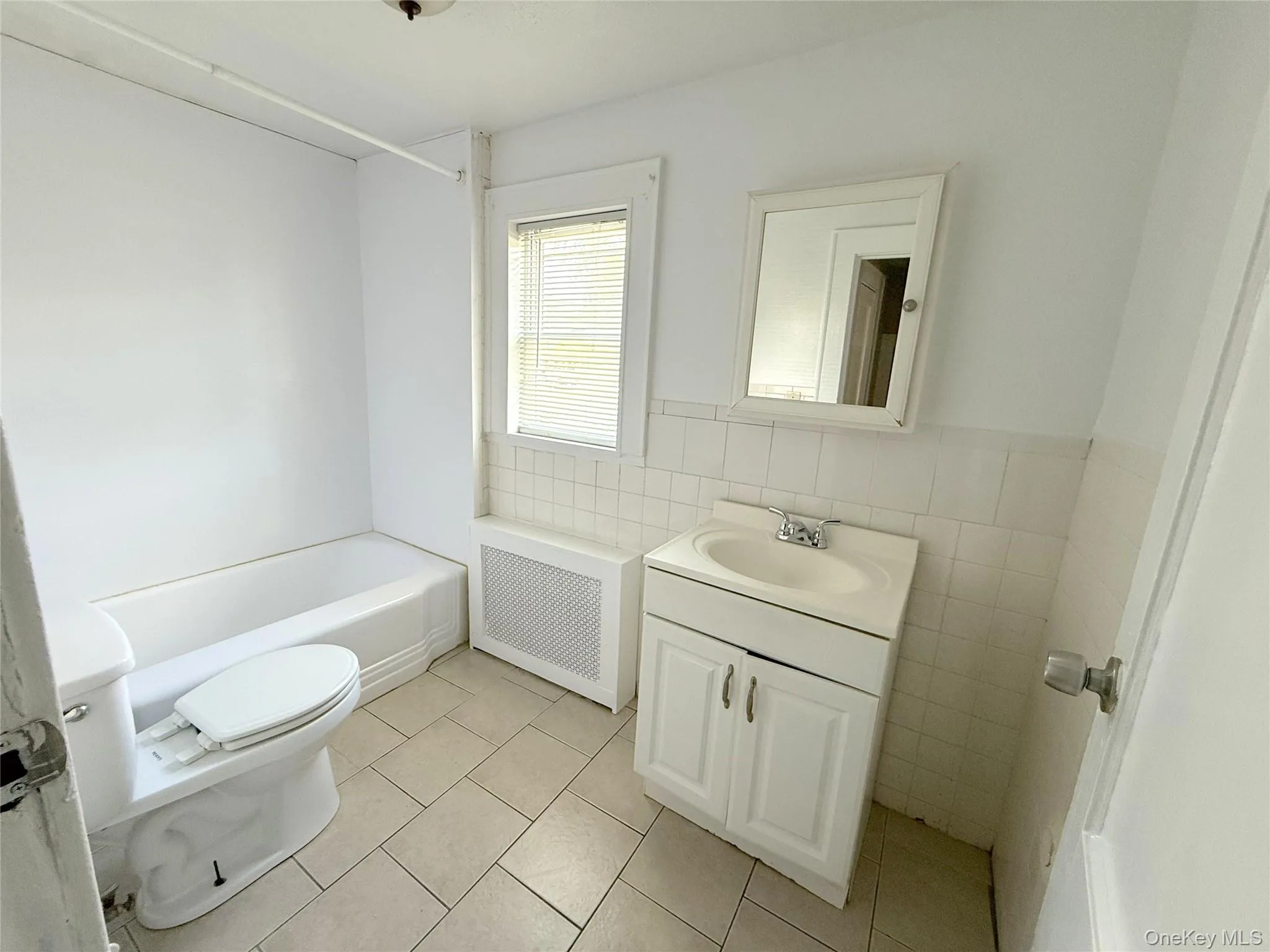 Full bathroom featuring radiator heating unit, vanity, tile walls, tile patterned flooring, and shower / bath combination Full bathroom featuring radiator heating unit, vanity, tile walls, tile patterned flooring, and shower / bath combination