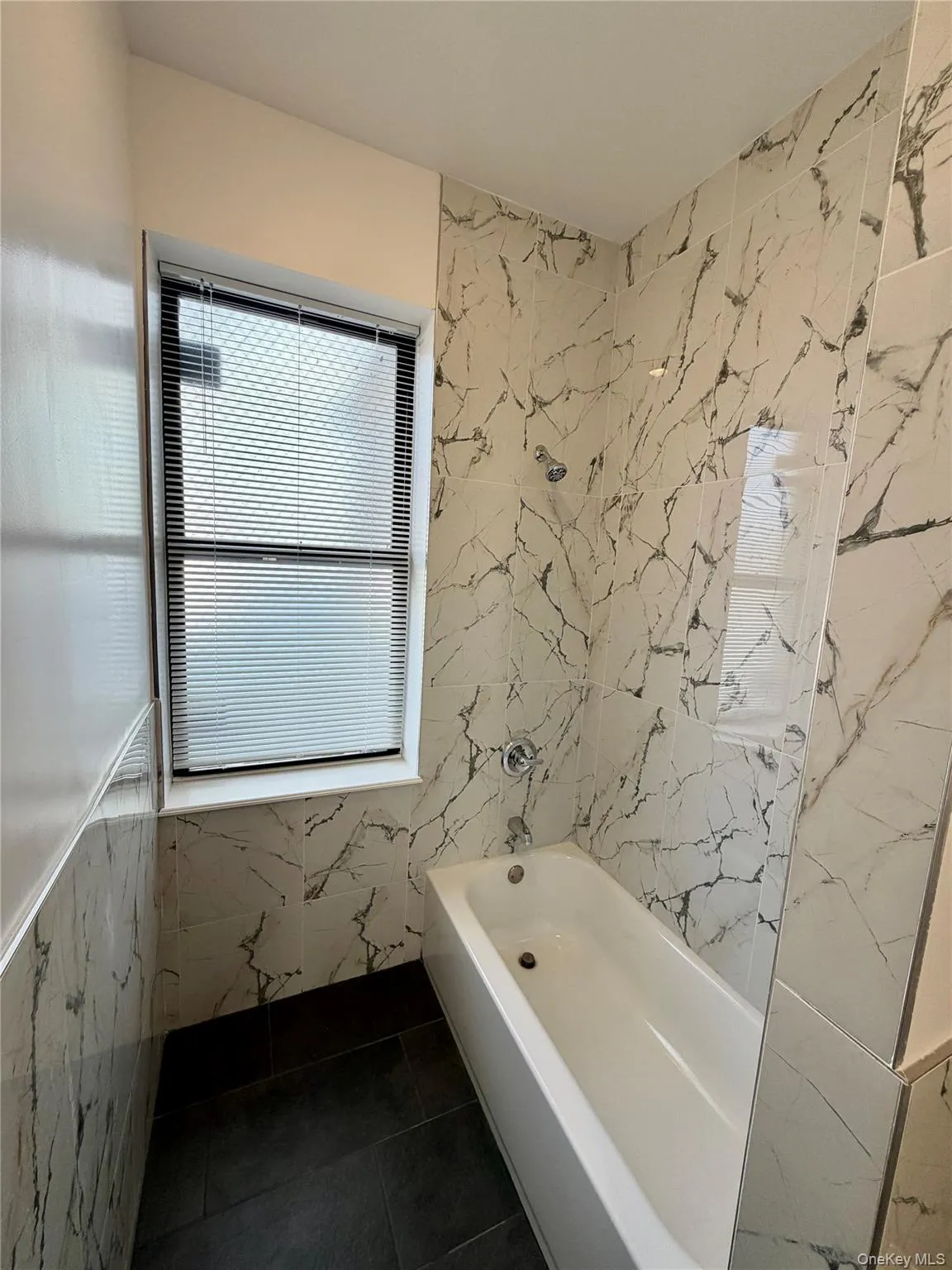 Bathroom featuring tile walls, a combined bath / shower with marble appearance, and dark tile patterned flooring Bathroom featuring tile walls, a combined bath / shower with marble appearance, and dark tile patterned flooring